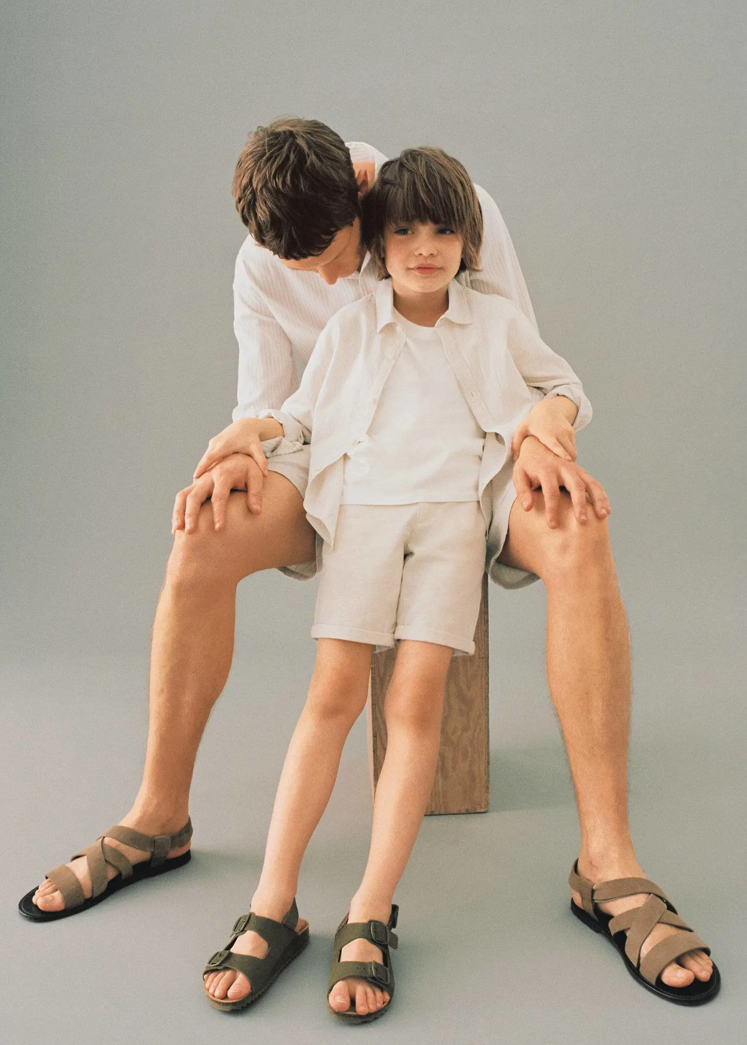 Mango KIDS/ Leather buckle sandal. a man and a boy sitting on top of a wooden block. 