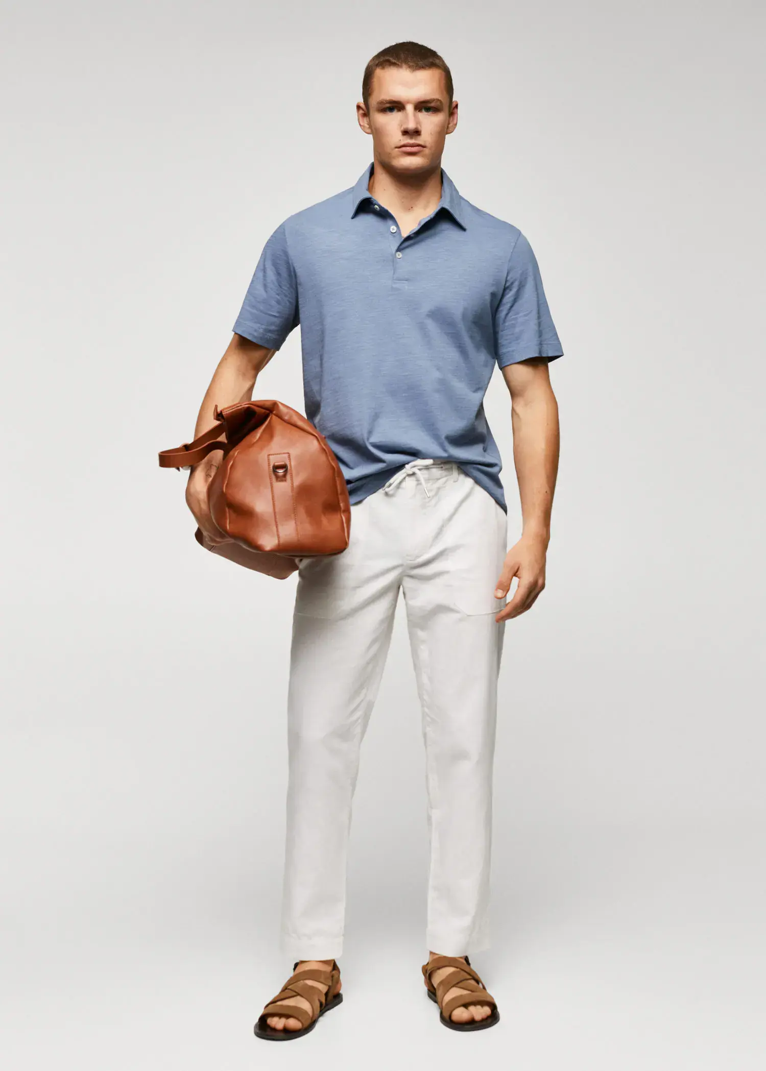 Mango 100% cotton basic polo shirt . a man holding a brown bag in front of a white wall. 