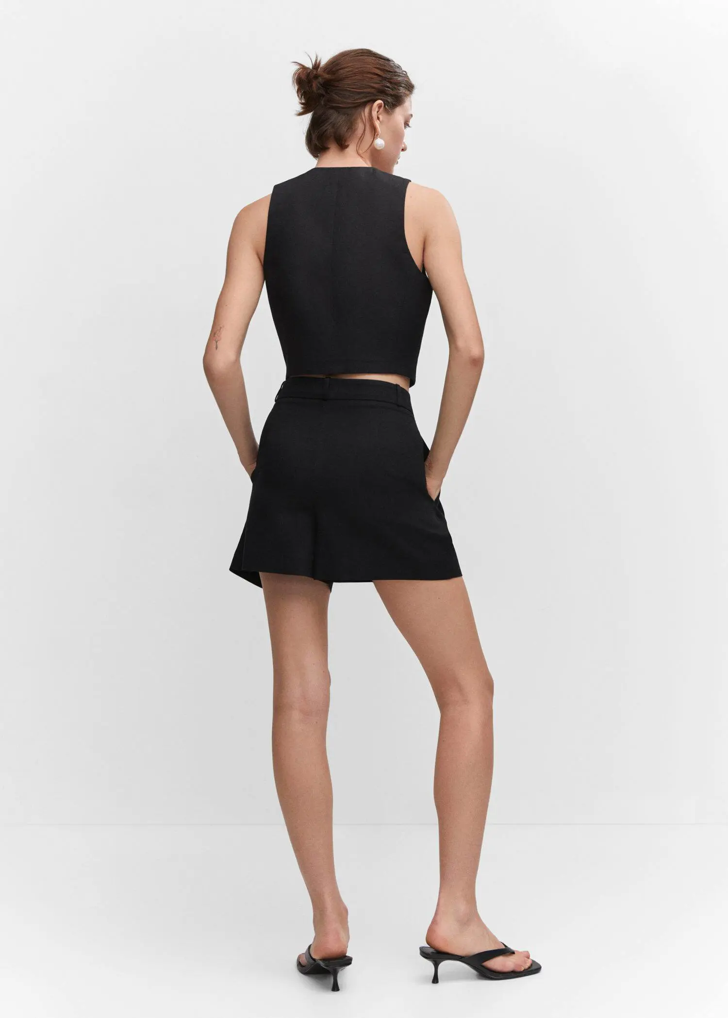 Mango Pleated high-waist shorts. a woman in a black outfit is standing with her hands in her pockets. 