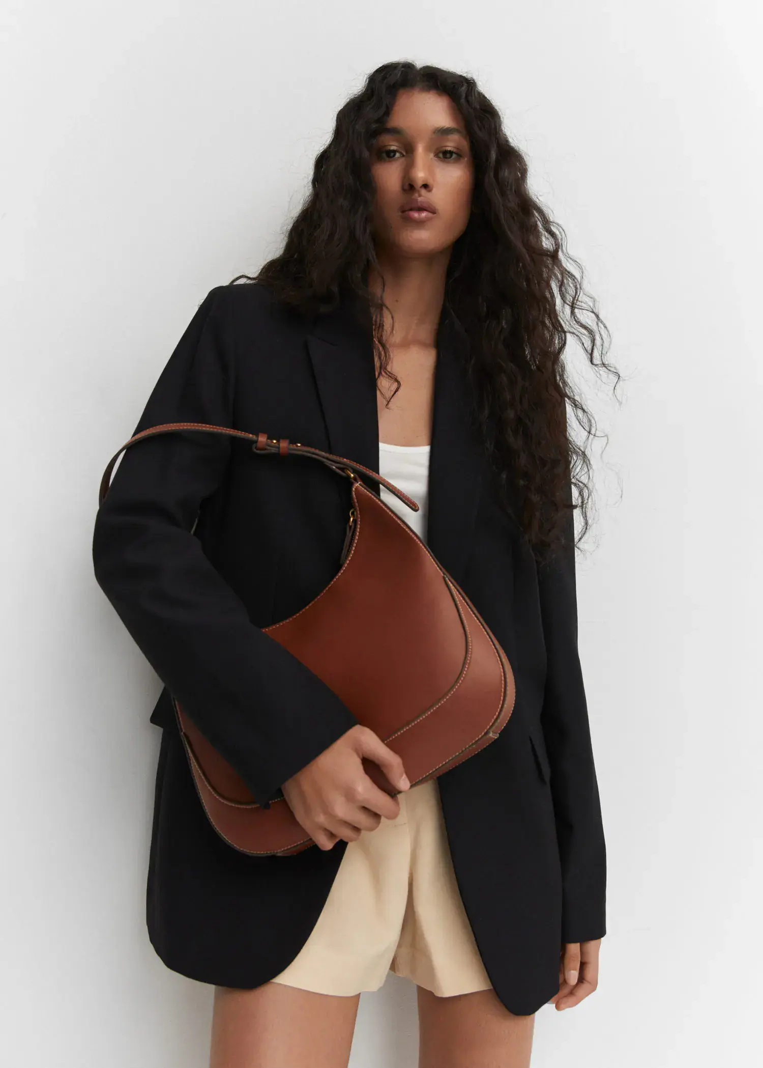 Mango Short-handle shoulder bag. a woman holding a brown purse in front of a white wall. 