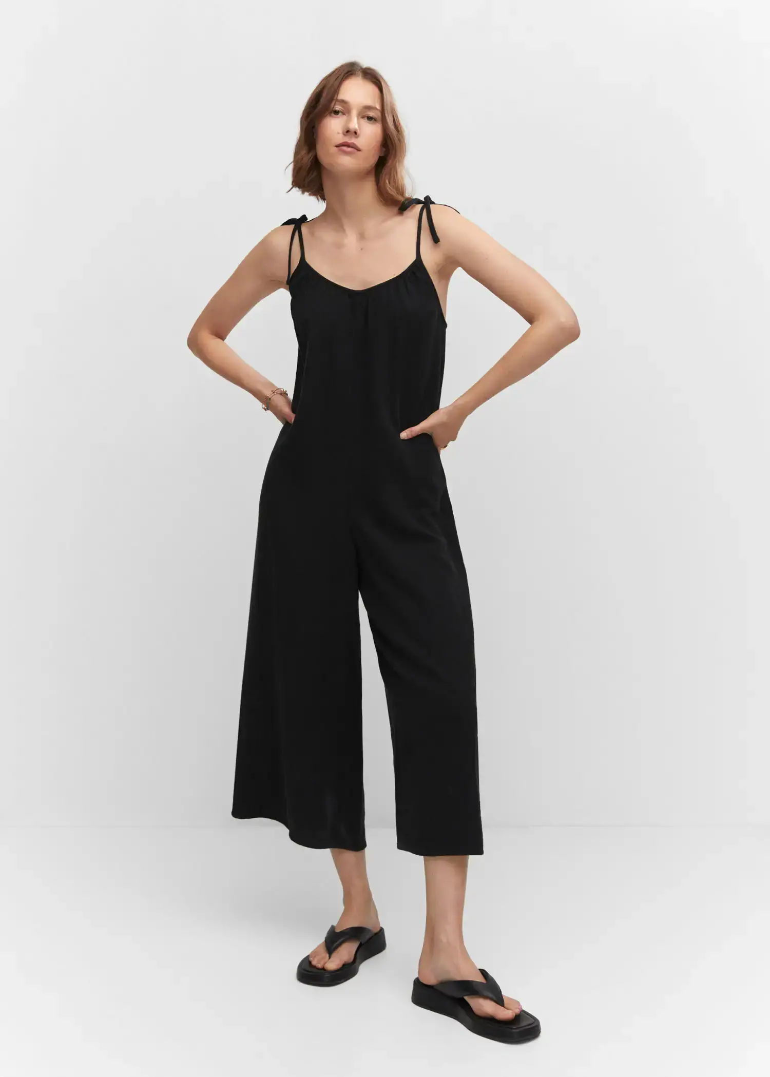 Mango Textured jumpsuit with bows. a woman wearing a black jumpsuit posing for a picture. 