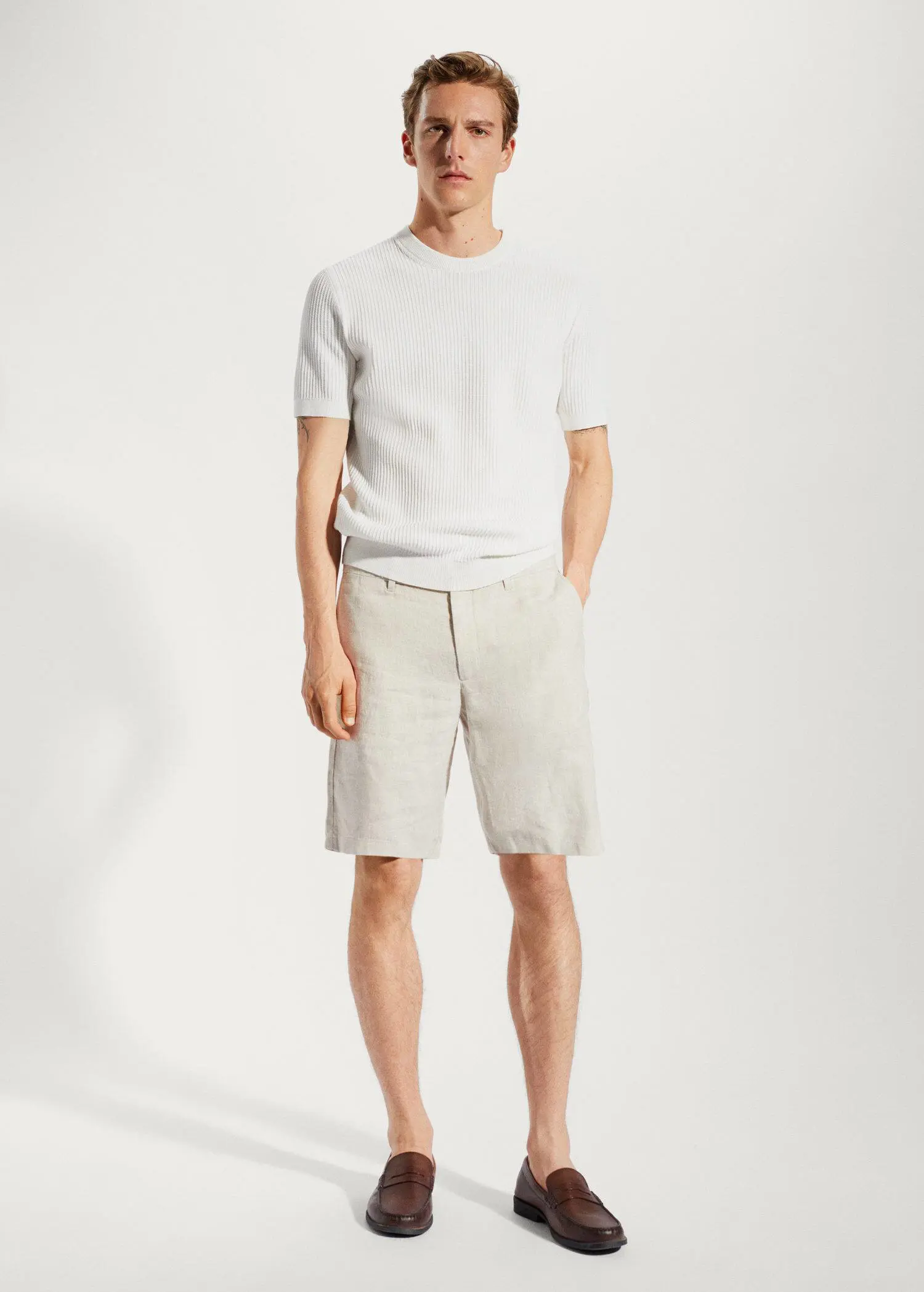 Mango 100% linen shorts. a man in white shirt and shorts standing in a room. 