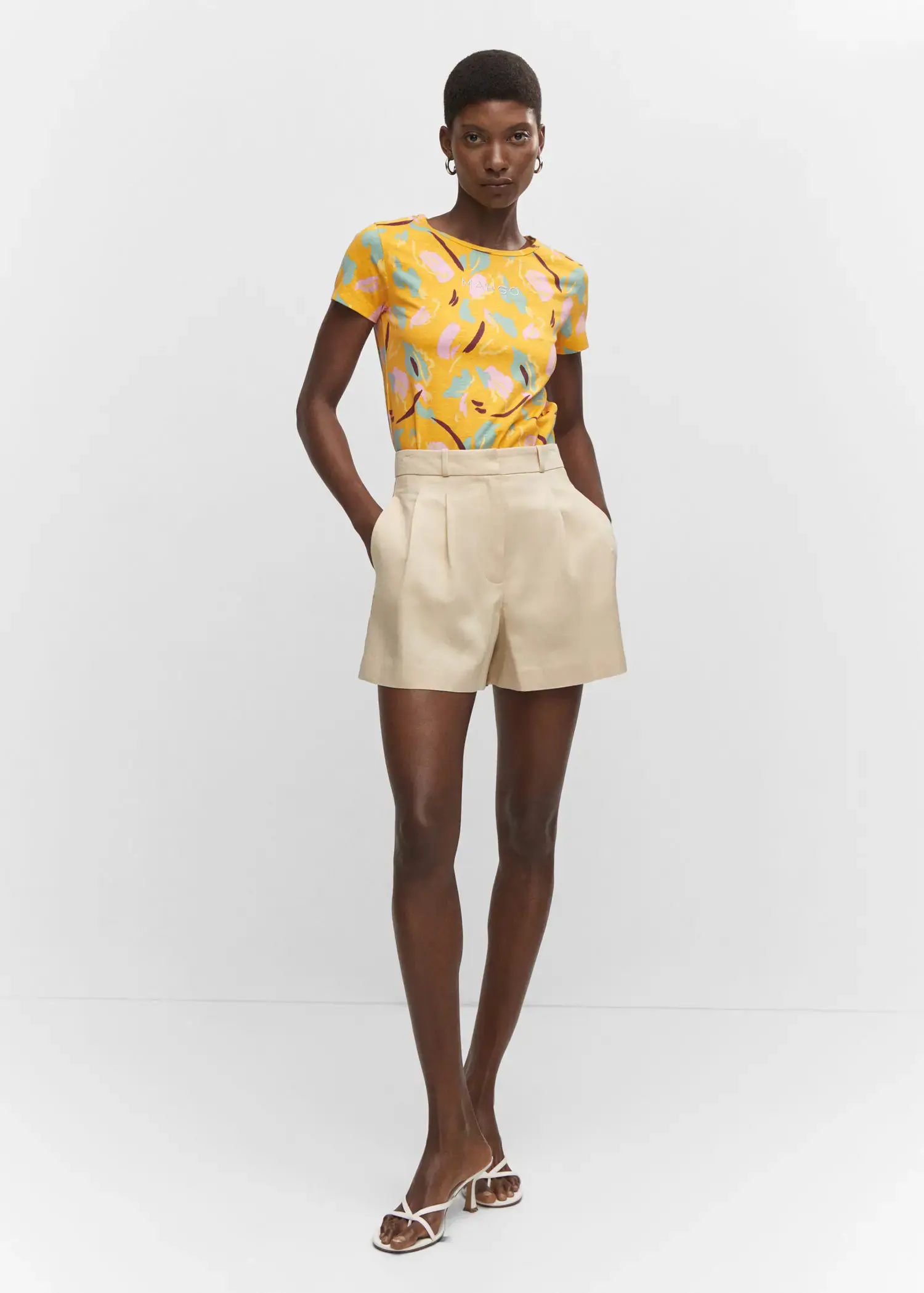 Mango Embroidered logo print t-shirt. a woman in a yellow top and beige shorts. 
