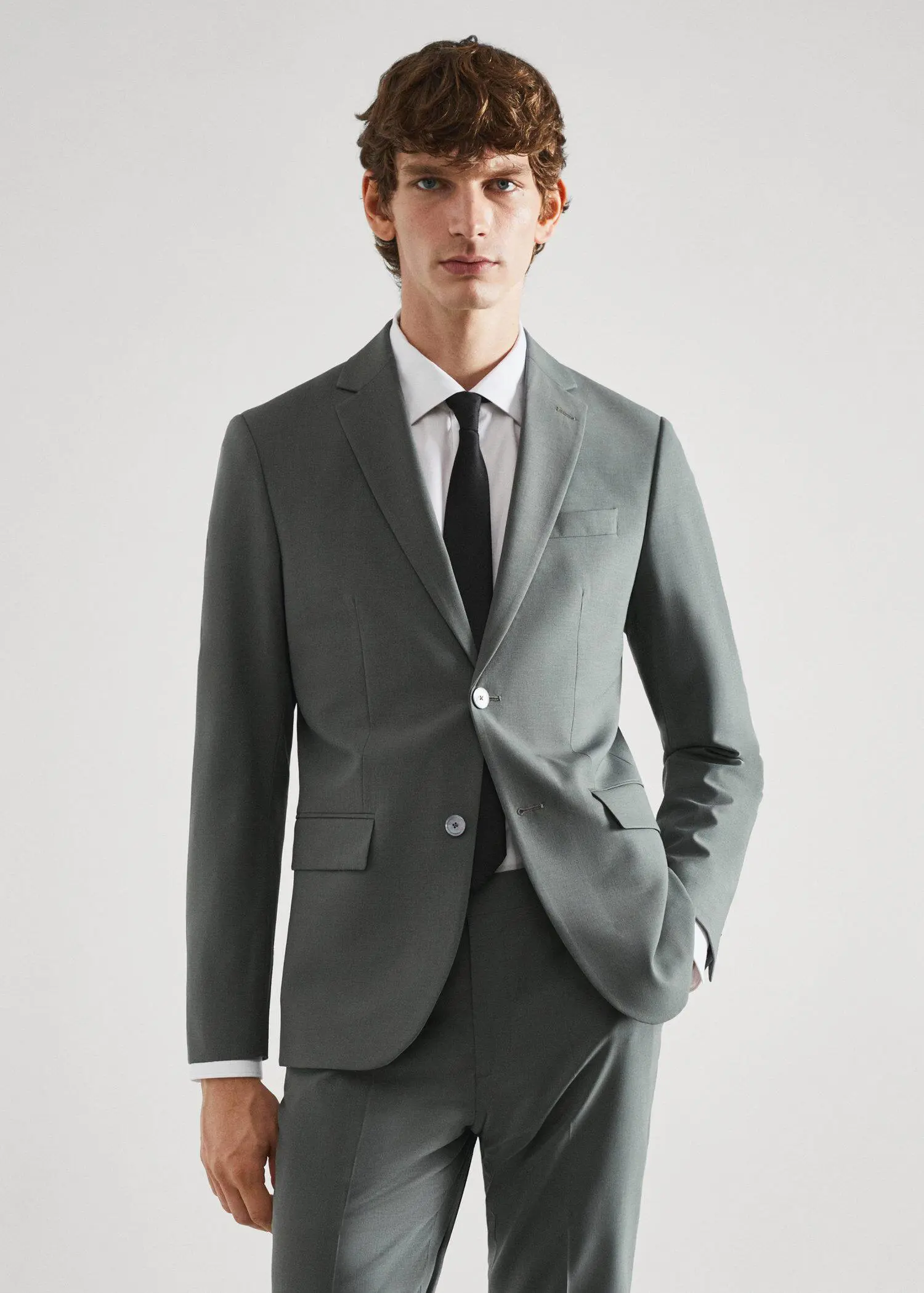 Mango Slim-fit wool suit blazer. a man wearing a suit and tie standing in front of a white wall. 