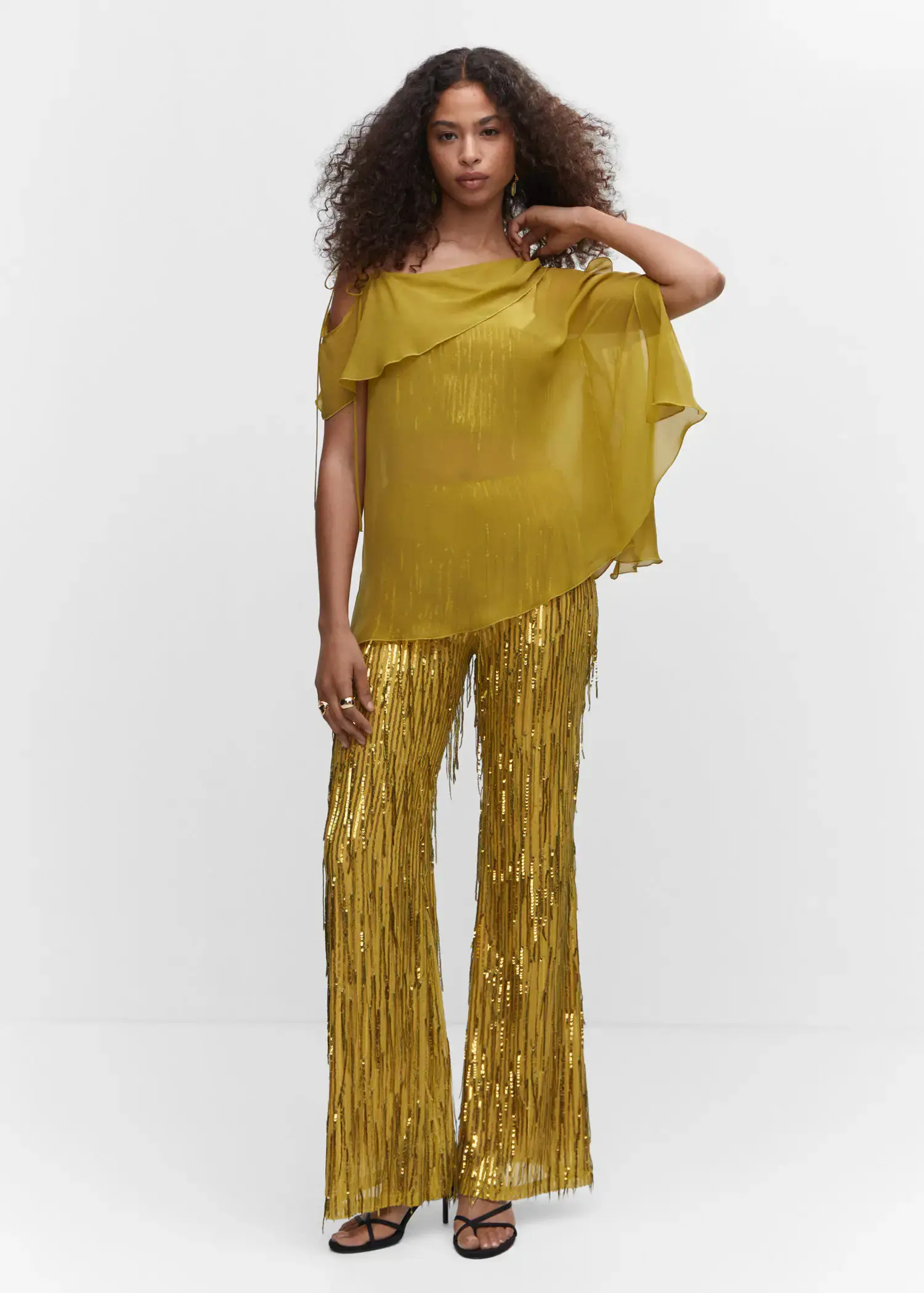 Mango Metallic fringed top. a woman in a yellow outfit standing in front of a white wall. 