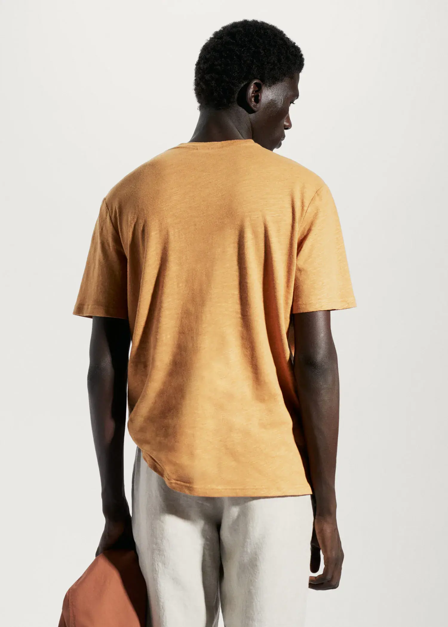 Mango Cotton-linen pocket t-shirt. a man in a yellow shirt is standing in front of a white wall. 