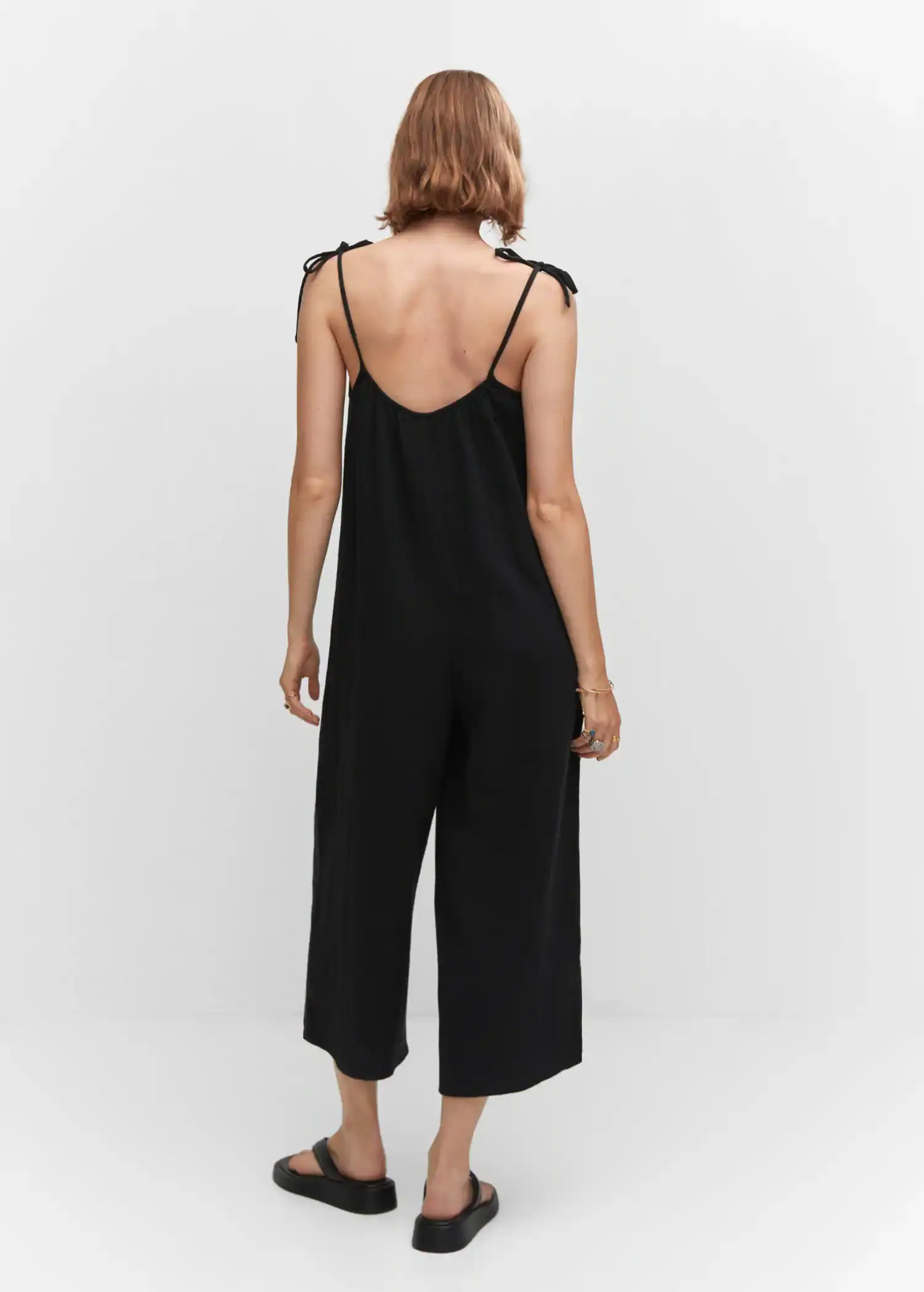 Mango Textured jumpsuit with bows. a woman wearing a black jumpsuit is standing in front of a wall. 