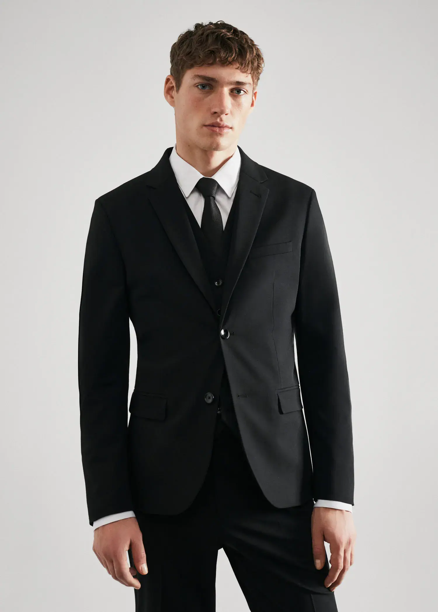Mango Super slim-fit suit blazer in stretch fabric. a man wearing a suit and tie standing in front of a white wall. 