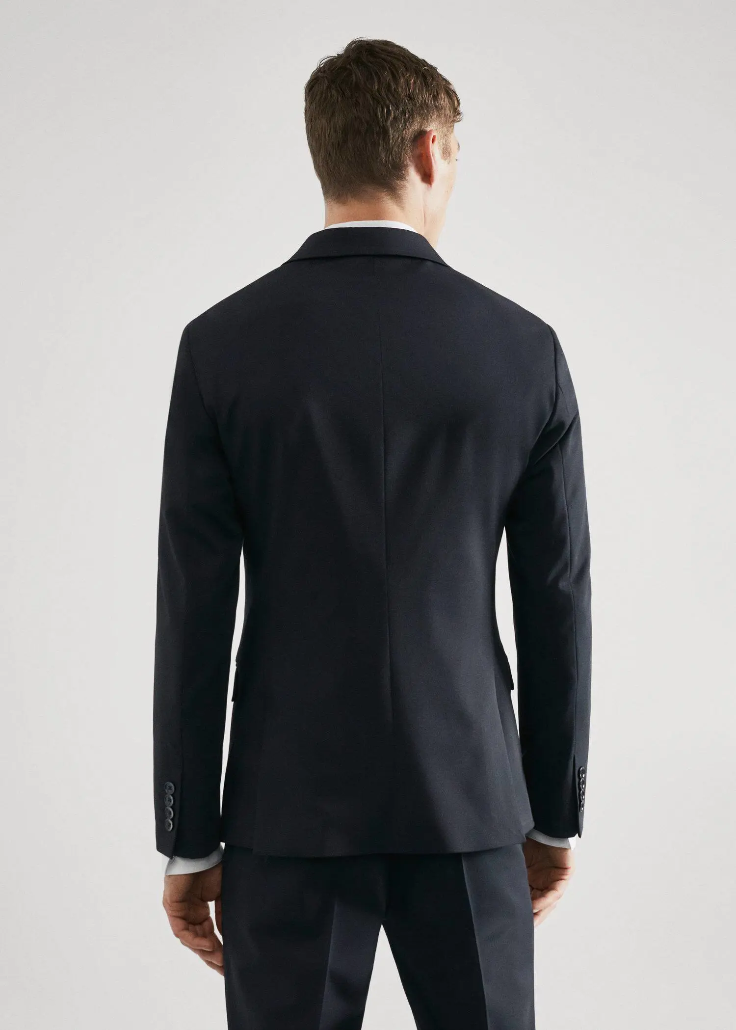 Mango Super slim-fit suit jacket in stretch fabric. a man wearing a black suit standing in front of a white wall. 