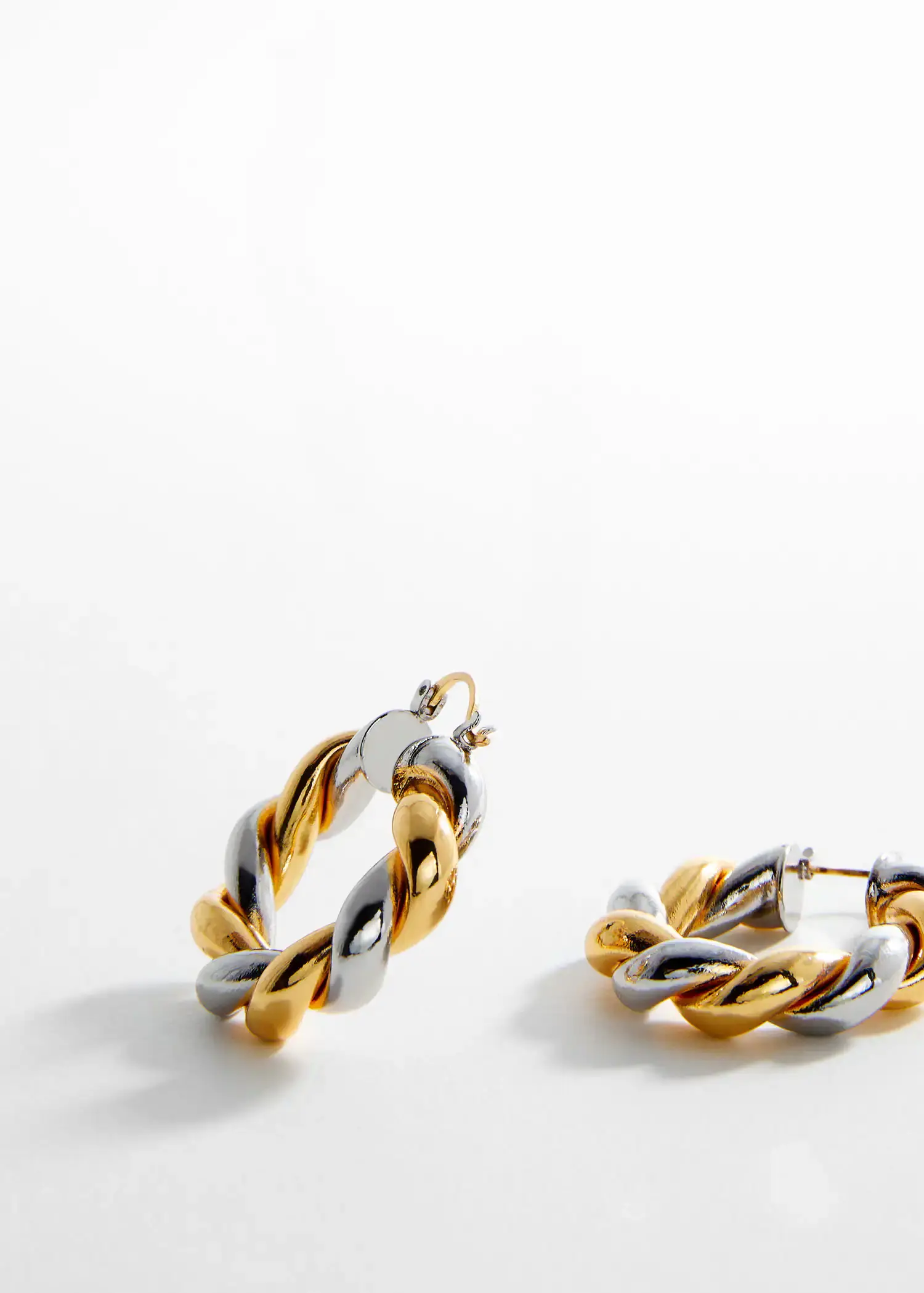 Mango Intertwined hoop earrings. a pair of gold and silver earrings on a table. 