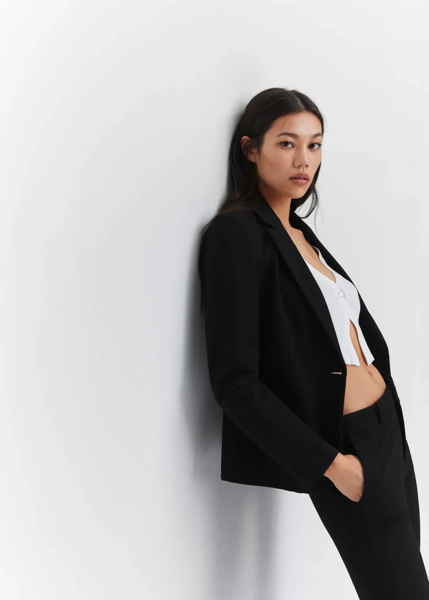 Mango Fitted blazer with blunt stitching. a woman wearing a black suit leaning against a wall. 