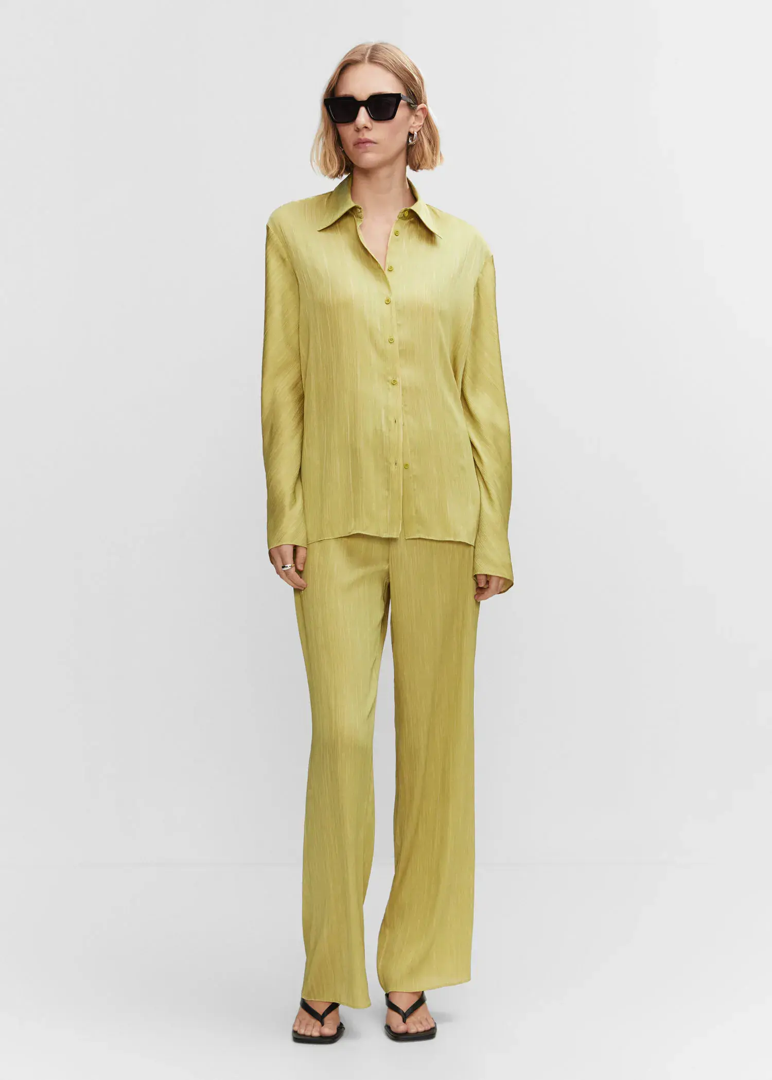 Mango Satin pleated shirt. a woman in a yellow outfit standing in front of a white wall. 