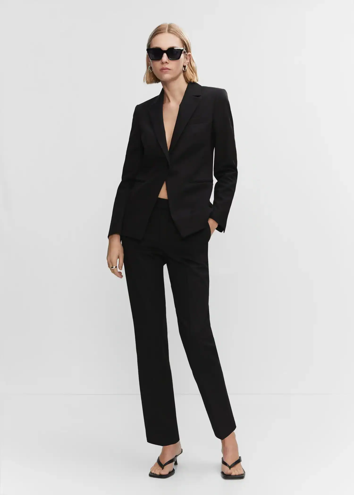 Mango Fitted suit blazer. a woman in a black suit standing in front of a white wall. 