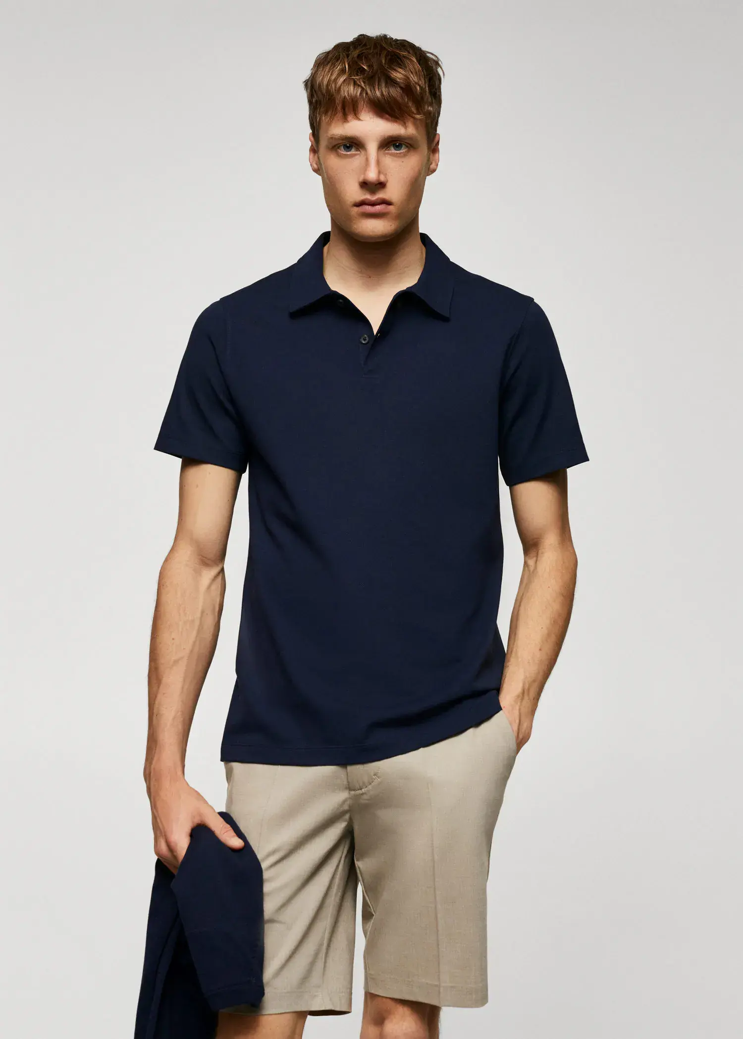 Mango Slim-fit textured cotton polo shirt. a man in a navy blue polo shirt holding a hat. 