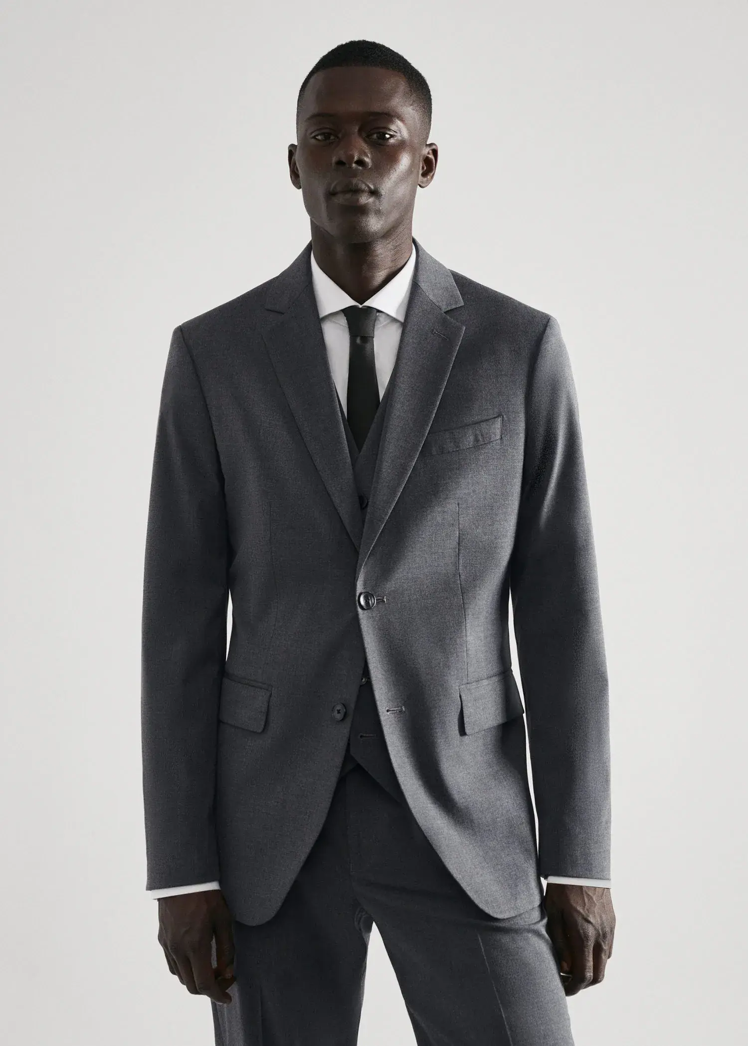 Mango Stretch fabric slim-fit suit jacket. a man wearing a suit and tie standing in front of a white wall. 