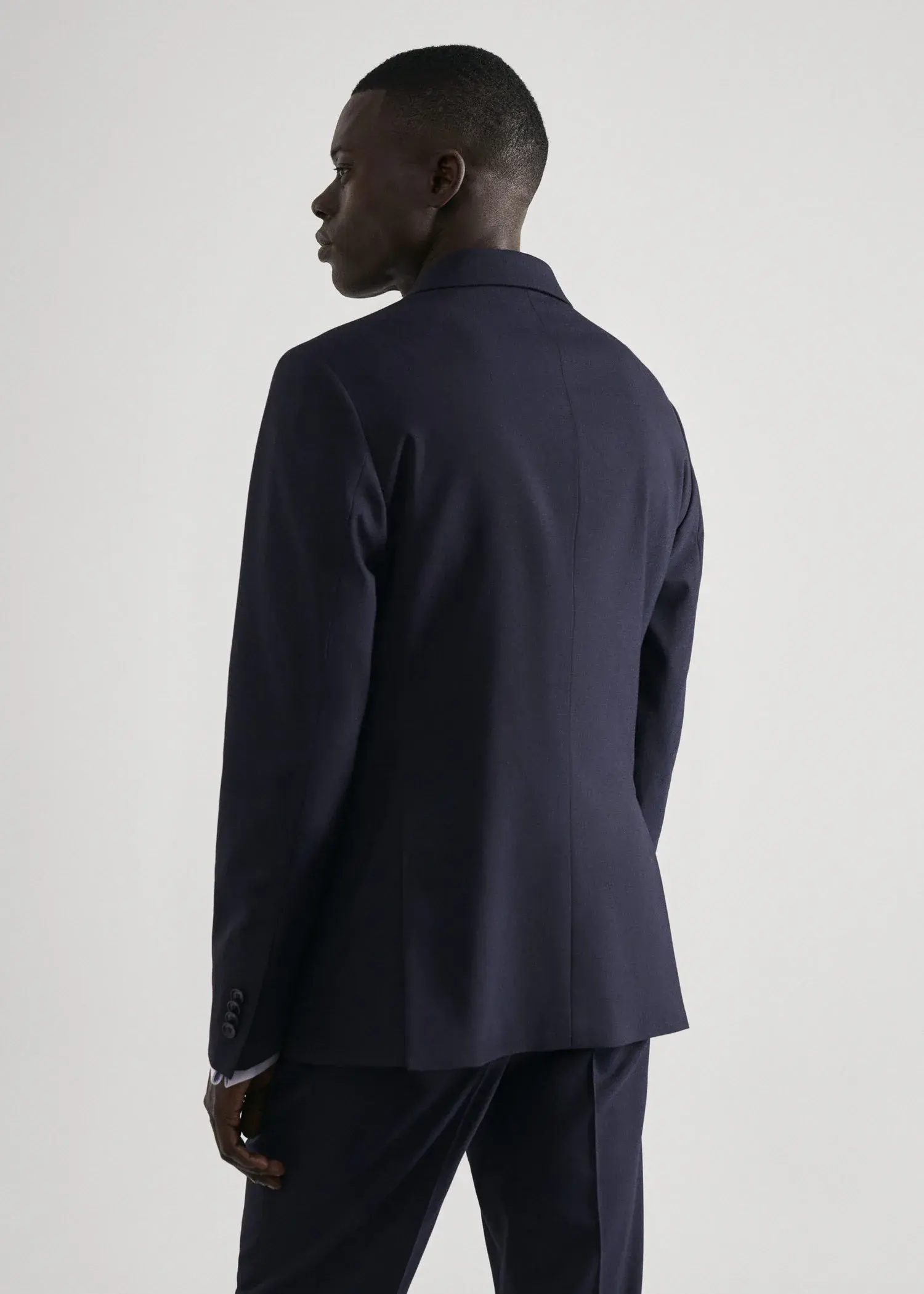 Mango Stretch fabric slim-fit suit jacket. a man wearing a suit standing next to a white wall. 