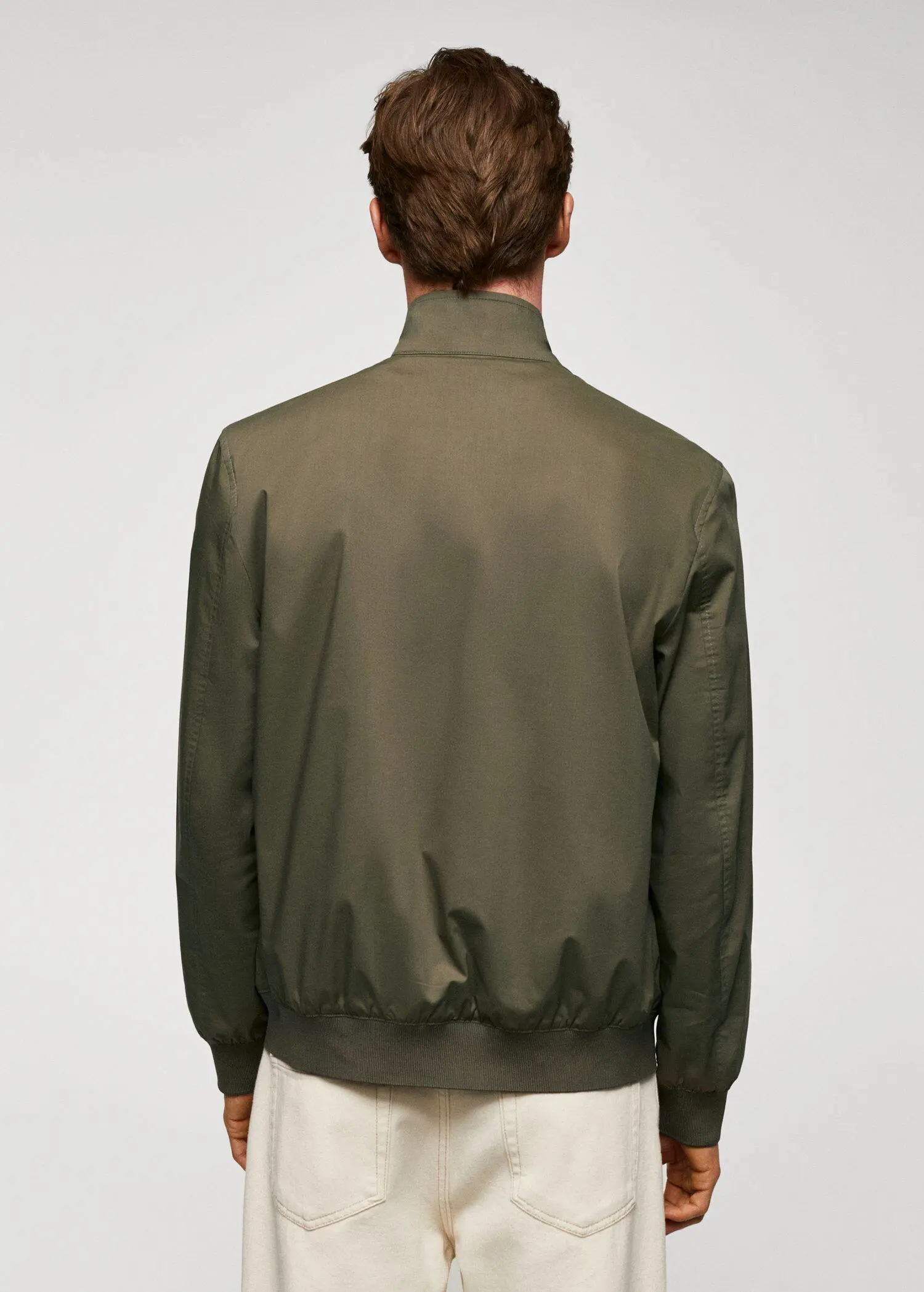 Mango Lightweight fabric bomber jacket. a man wearing a green jacket standing in front of a white wall. 