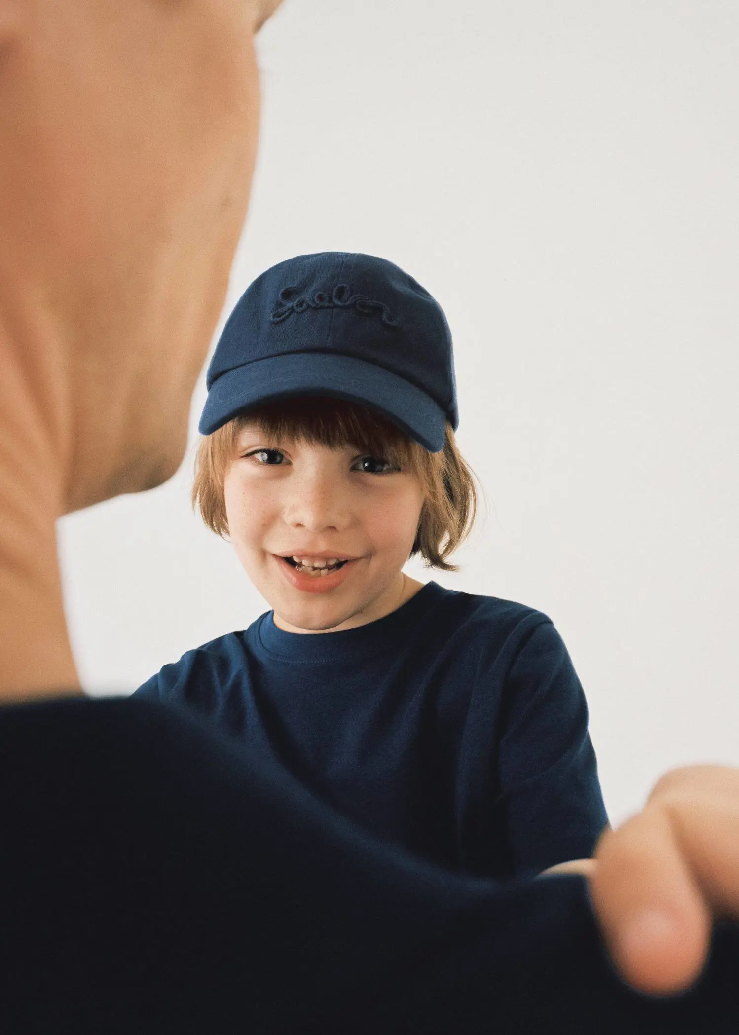 Mango  KIDS/ Embroidered cotton cap. a young boy wearing a blue hat looking at an older man. 