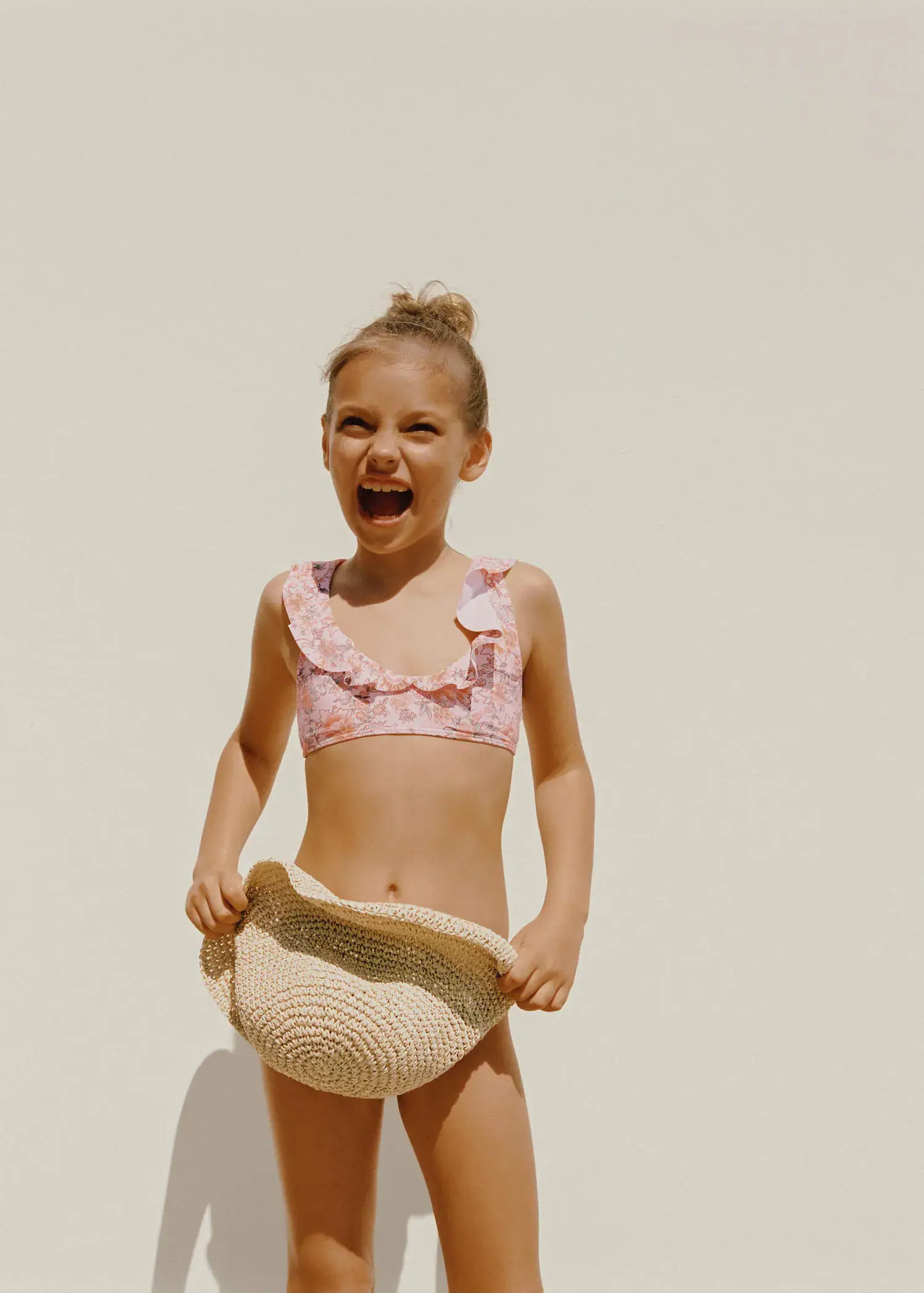 Mango KIDS/ Floral print bikini. a little girl in a pink bathing suit holding a straw hat. 