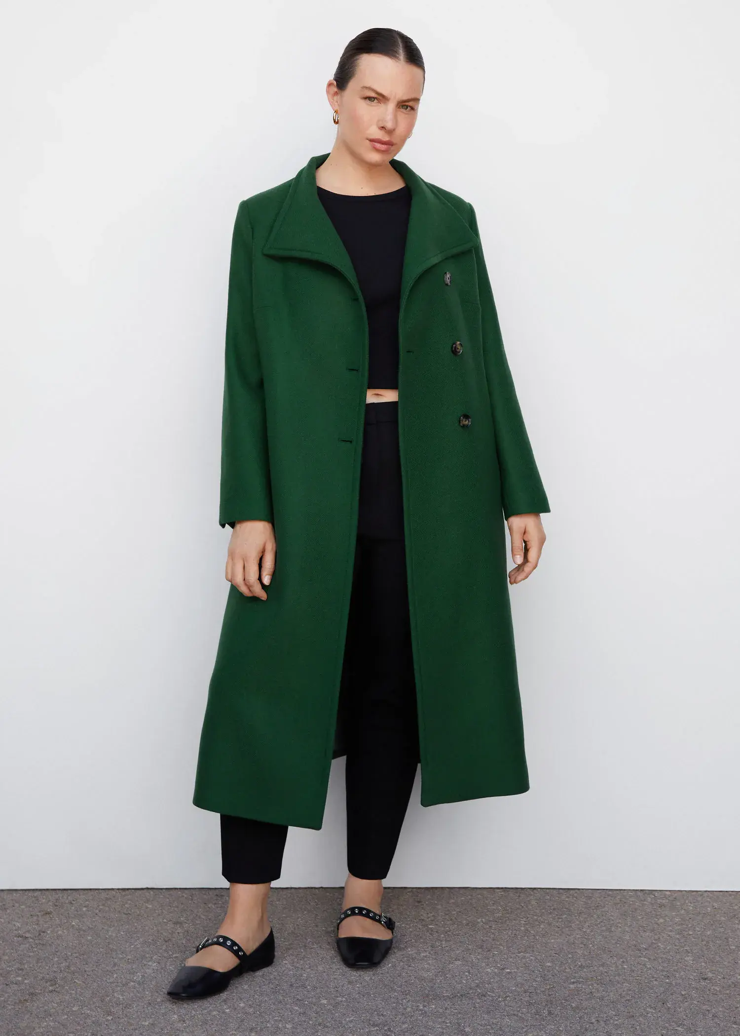 Mango Woollen coat with belt. a woman wearing a long green coat standing in front of a white wall. 