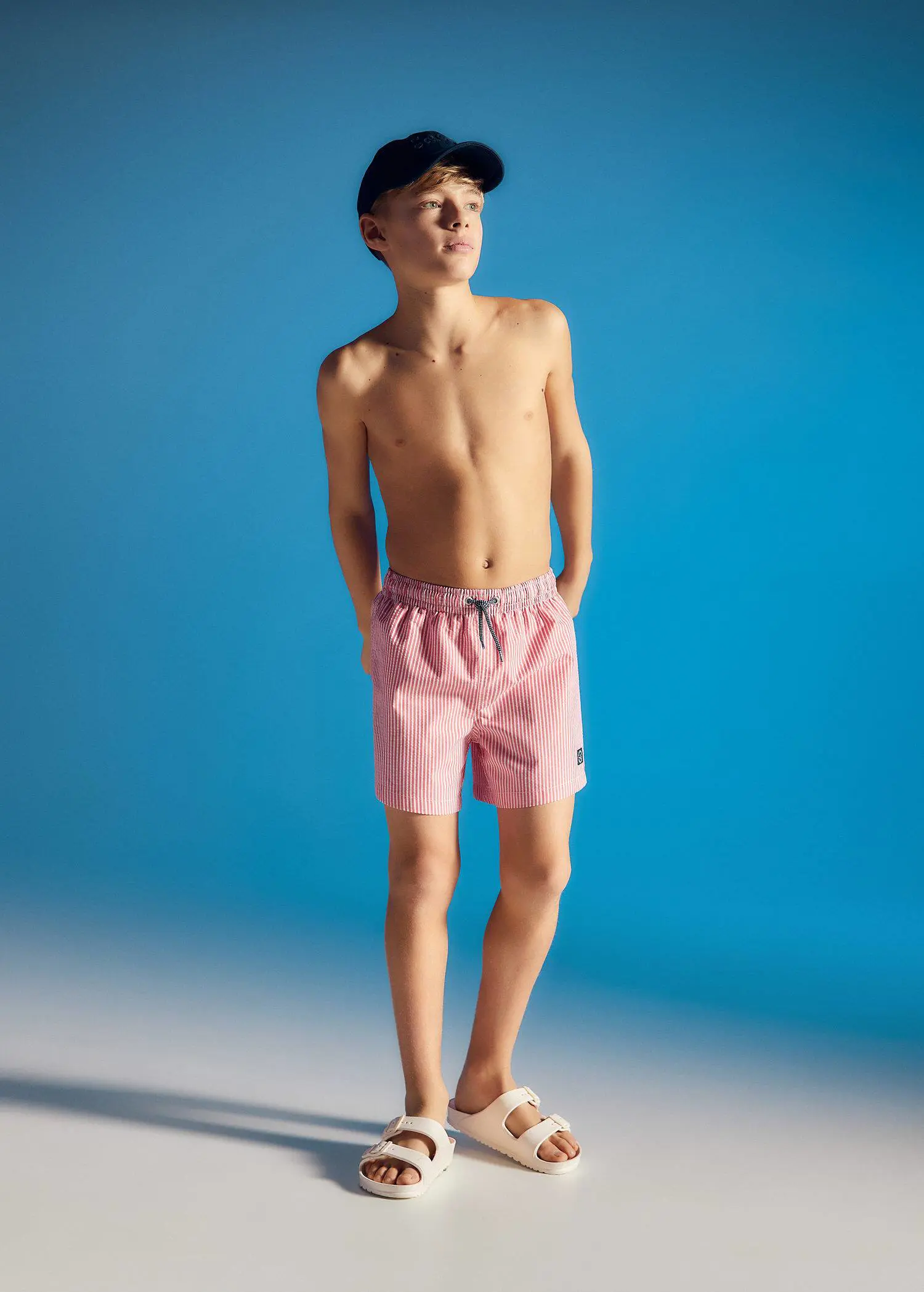 Mango KIDS/ Striped swimsuit. a young man standing in a pink swim trunks. 