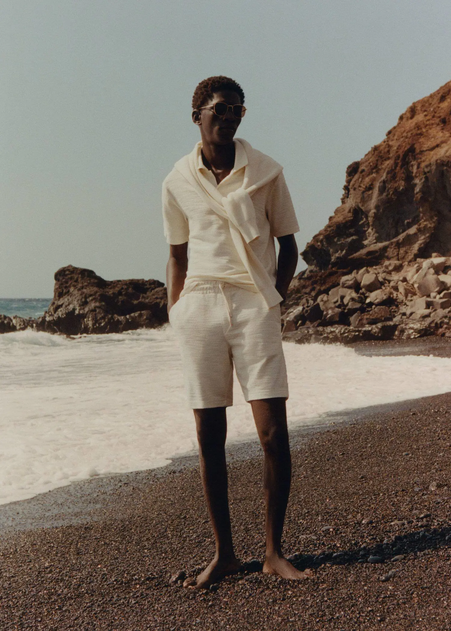 Mango Structured cotton Bermuda. a man standing on the beach wearing white shorts. 