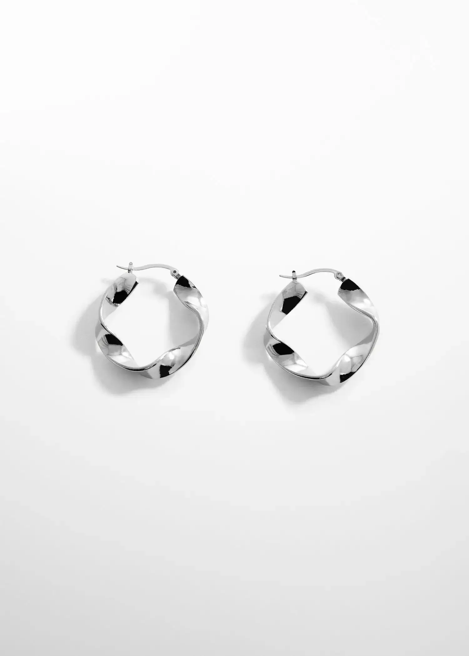 Mango Twisted hoop earrings. a pair of silver earrings on top of a white wall. 
