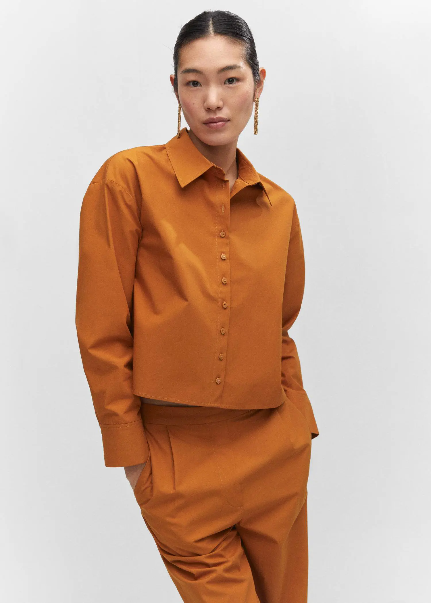Mango 100% cotton crop shirt. a woman in a brown outfit standing in front of a white wall. 