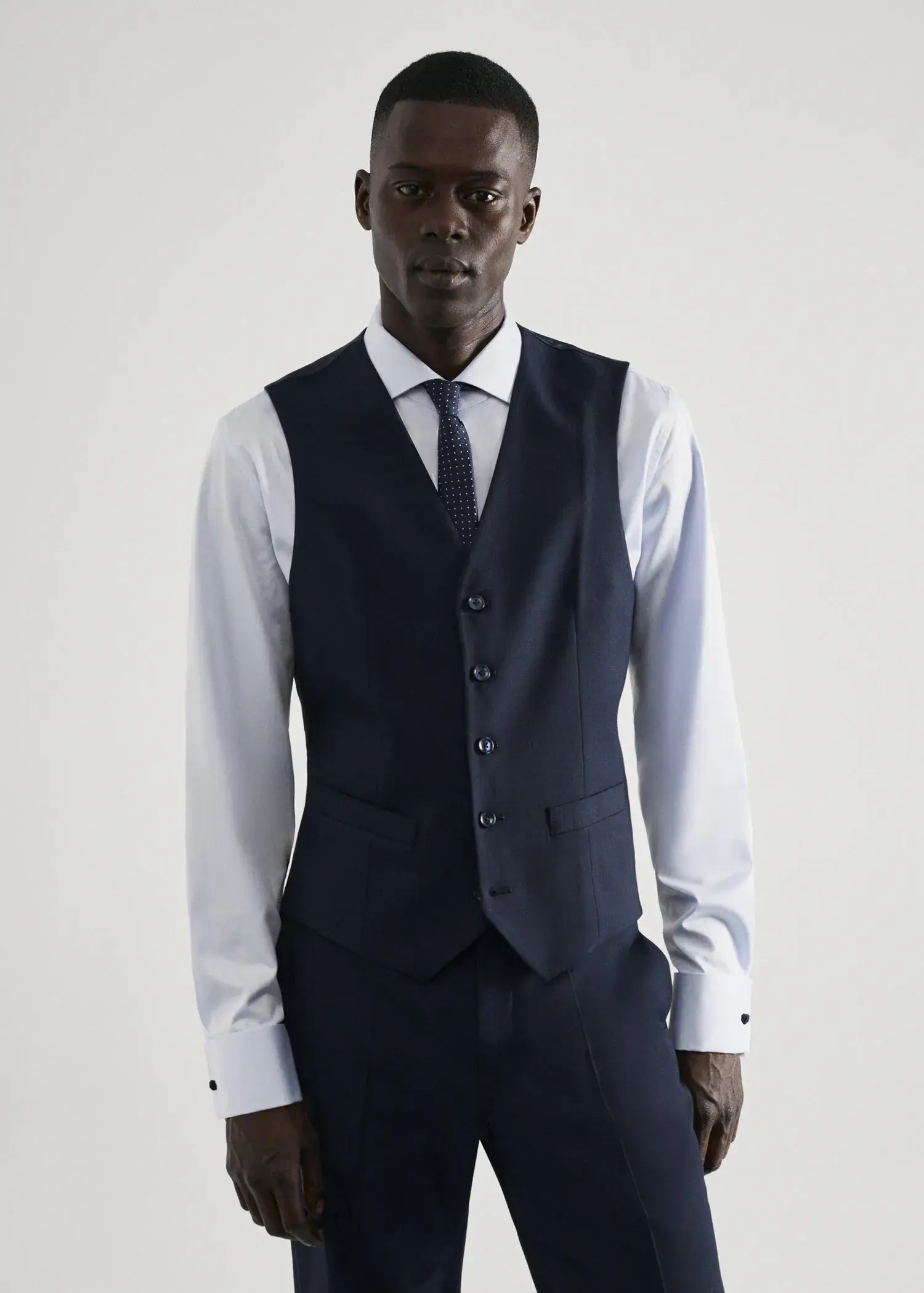 Mango Slim-fit suit waistcoat. a man wearing a suit and tie standing in front of a white wall. 
