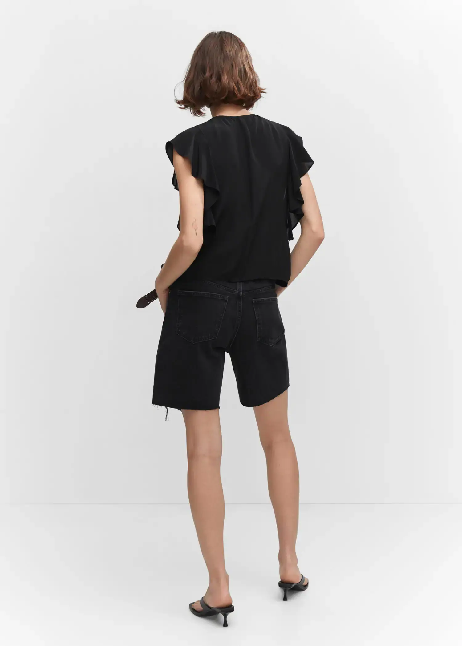 Mango Ruffled blouse. a woman in black shorts and a black top. 