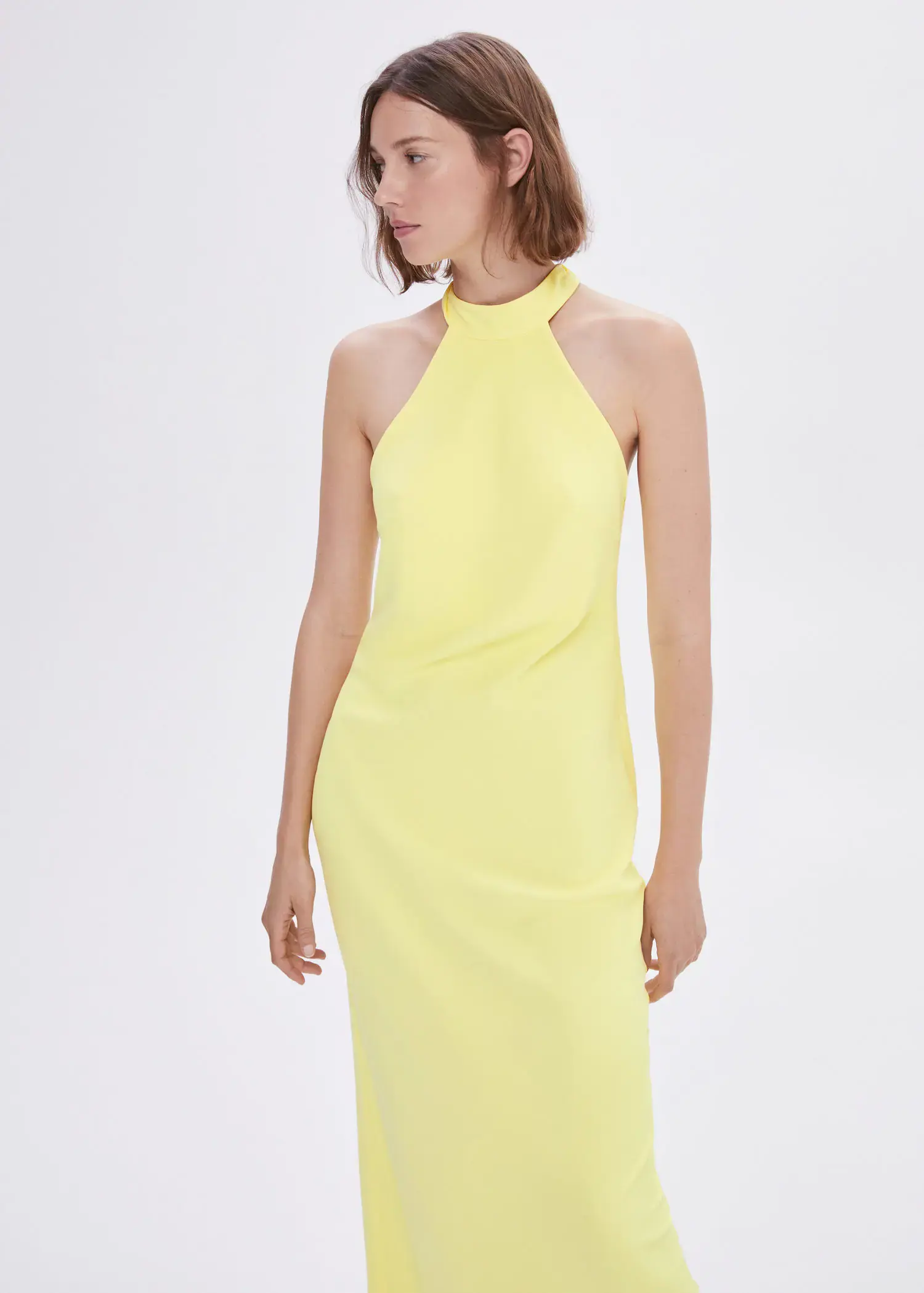 Mango Halter-neck open-back dress. a woman wearing a yellow dress standing in front of a white wall. 