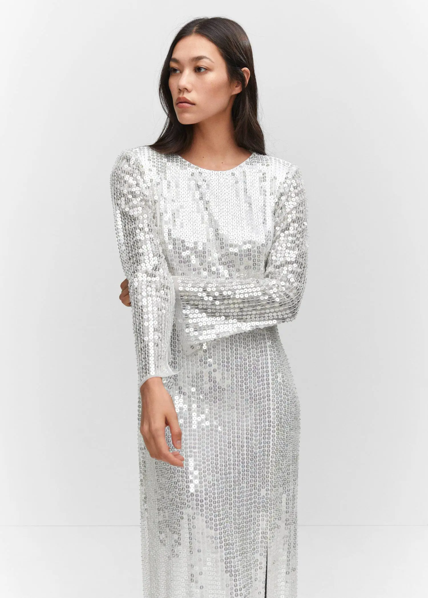 Mango Side slit sequined gown. a woman wearing a silver dress standing in front of a white wall. 