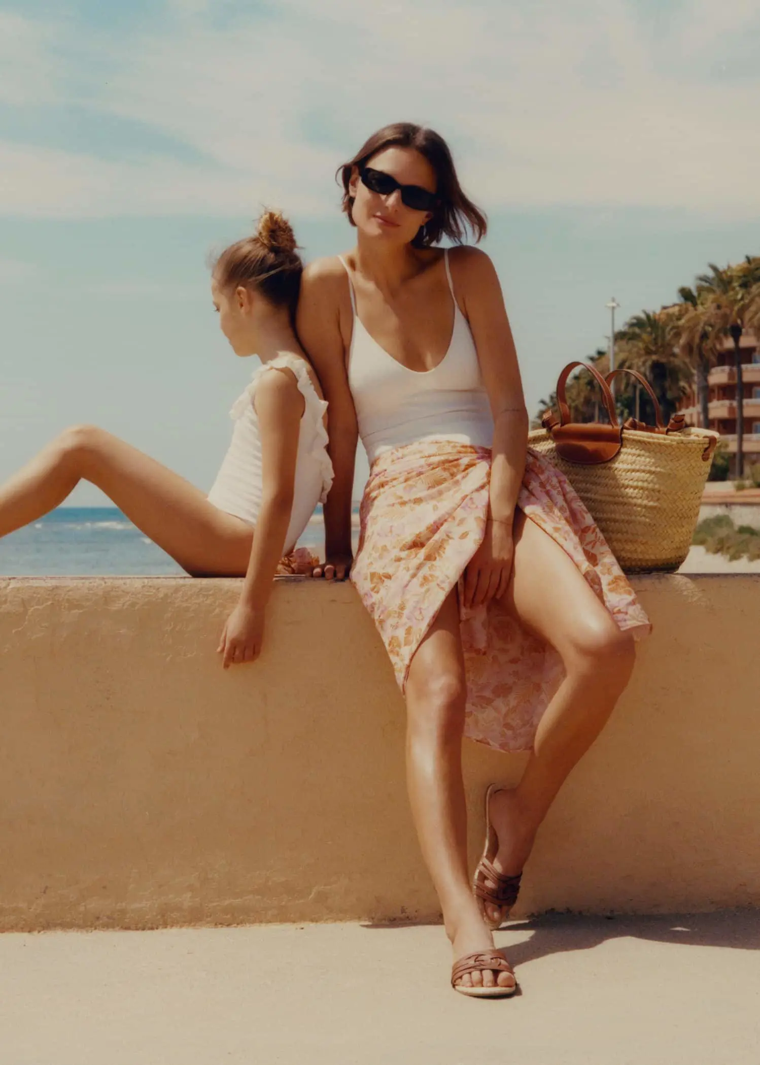 Mango Texture ruffle swimsuit. two young women sitting on a wall near the ocean. 