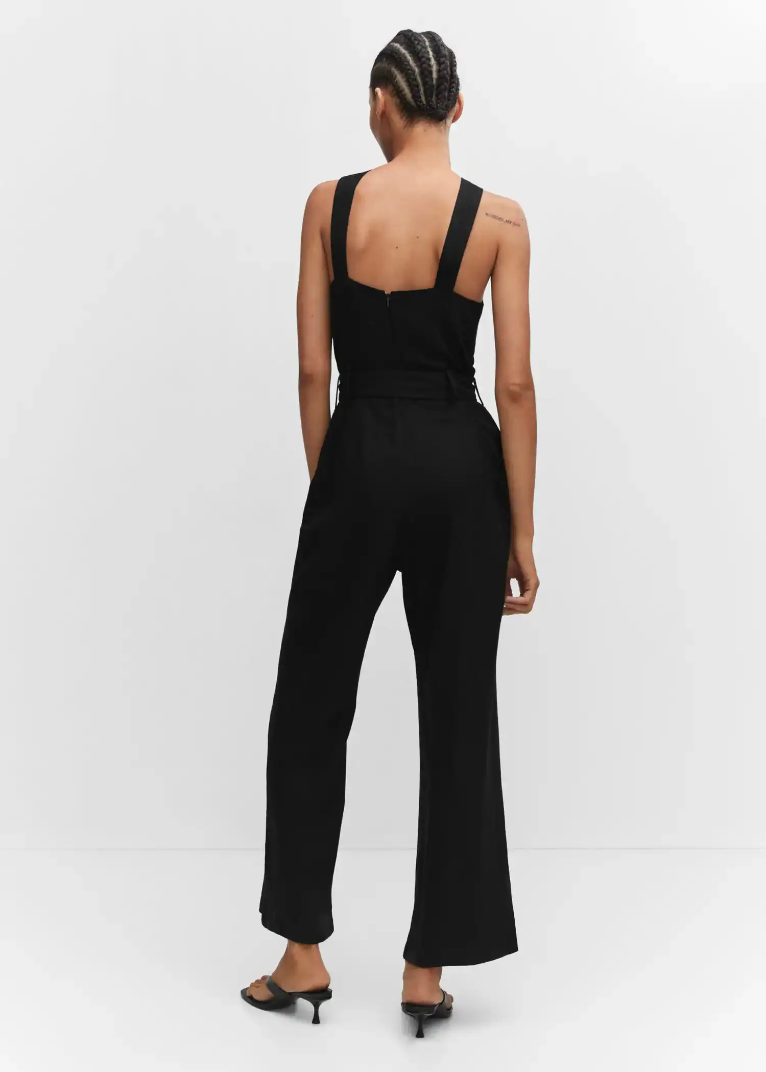 Mango Halter-neck jumpsuit with belt. a woman in a black jumpsuit is standing in front of a white wall. 
