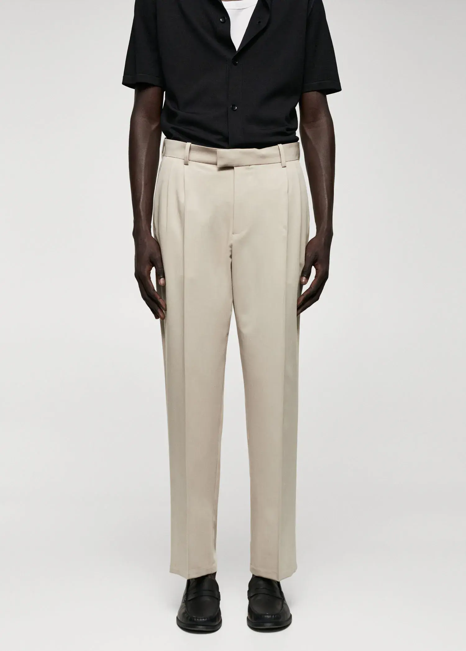 Mango Regular fit suit trousers with pleats. a man in a black shirt and beige pants. 