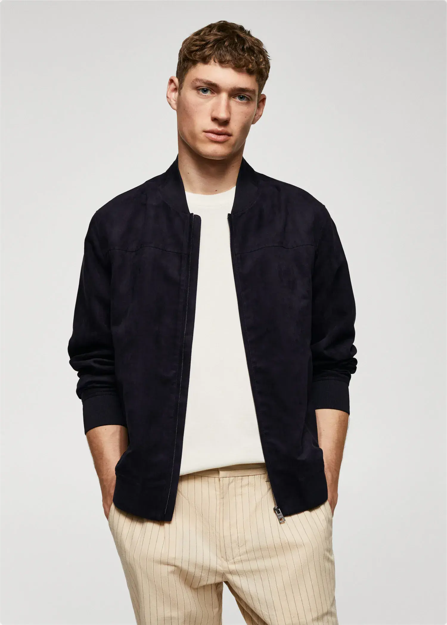 Mango Suede-effect bomber jacket. a man wearing a black jacket standing in front of a wall. 