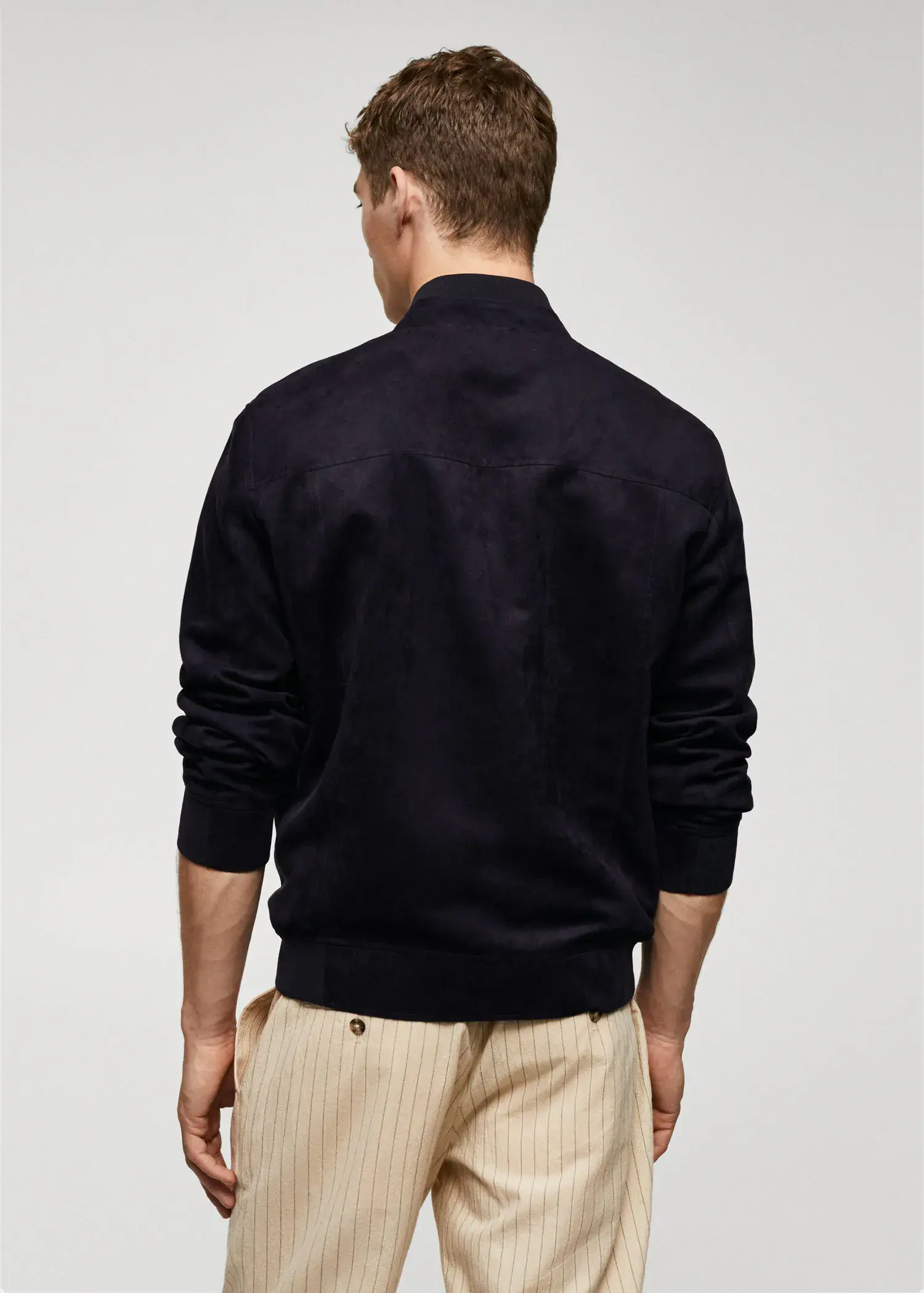 Mango Suede-effect bomber jacket. a man wearing a black jacket standing next to a wall. 
