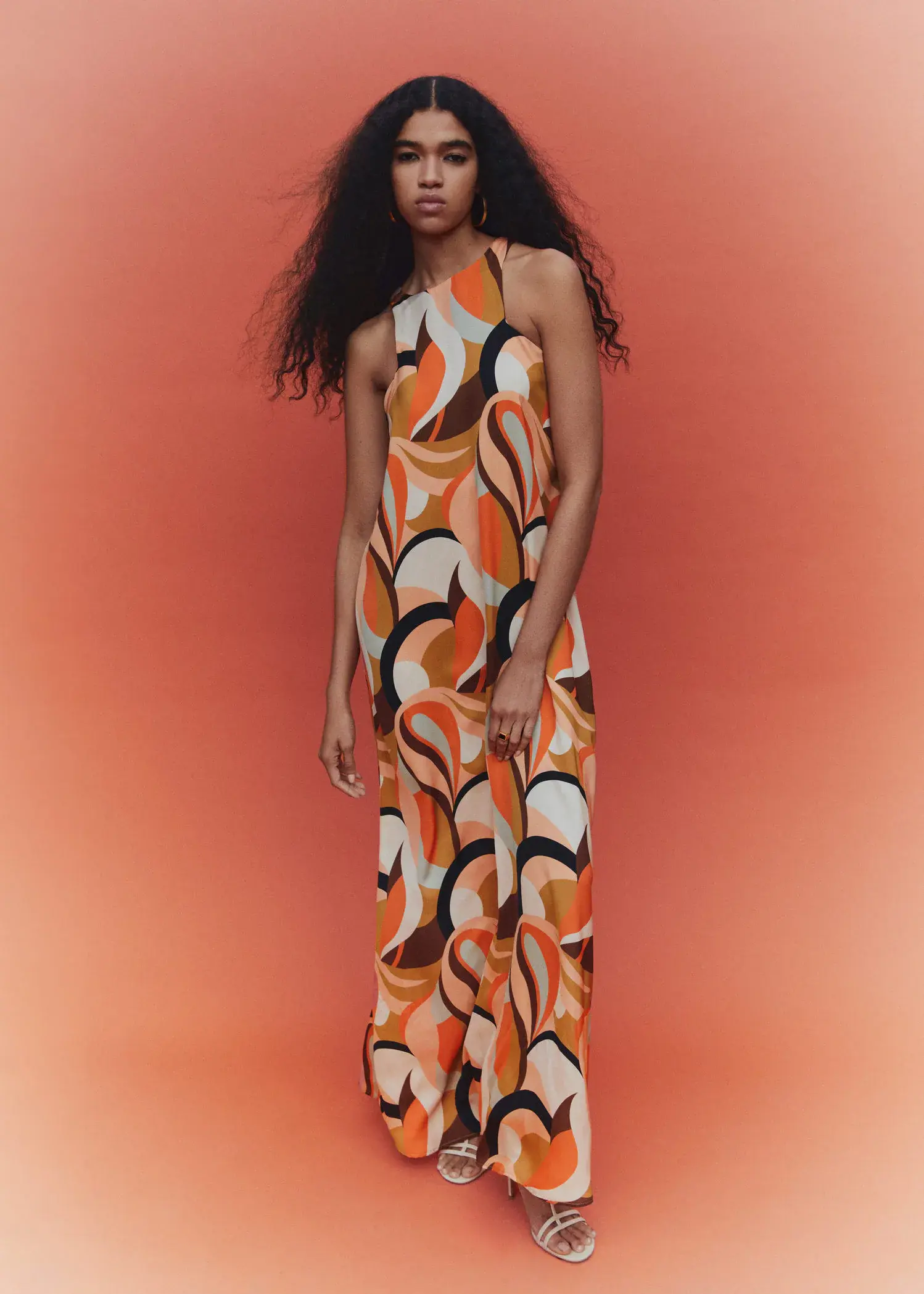 Mango Printed halter gown. a woman standing in front of an orange background. 