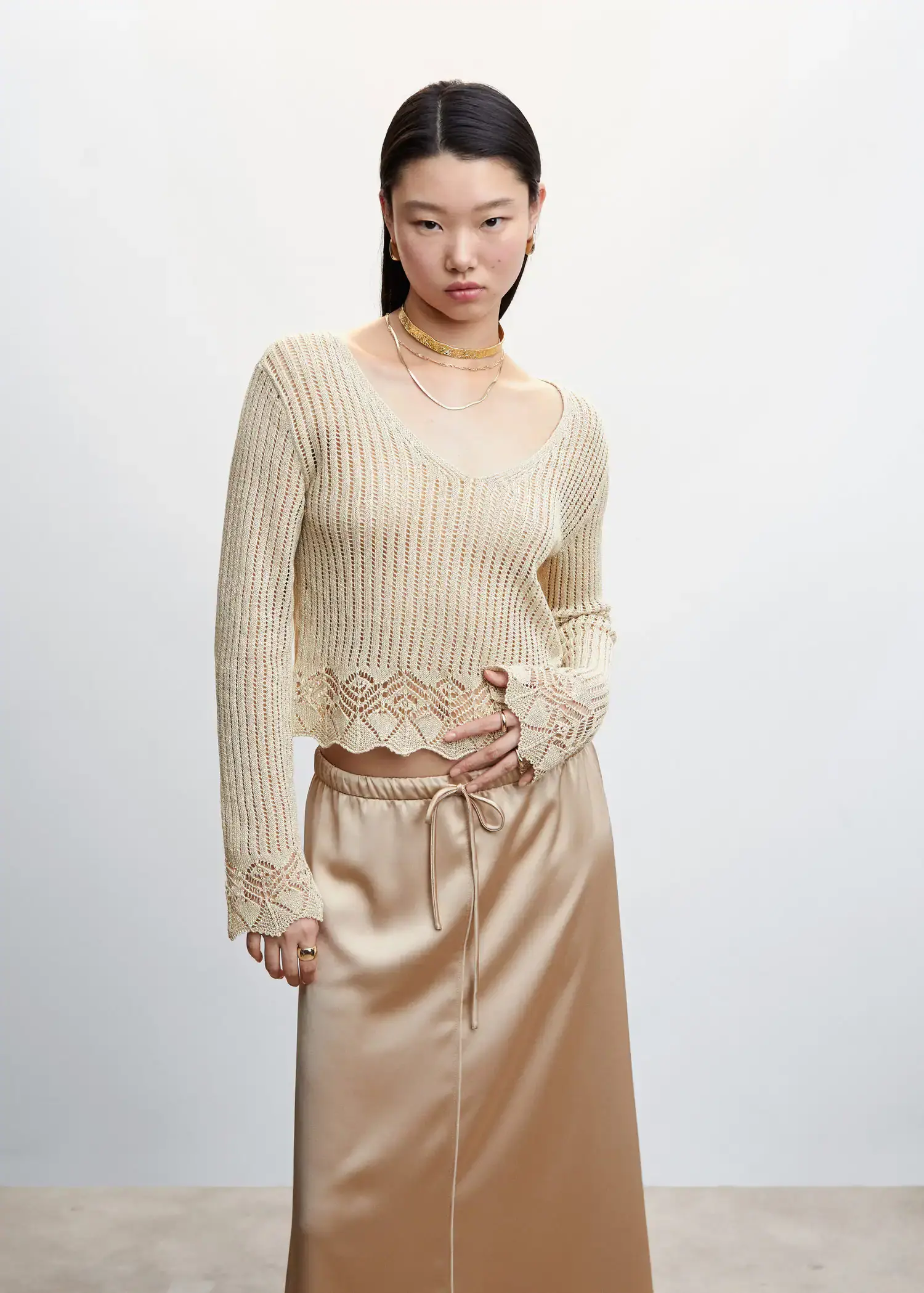 Mango Open work-detail sweater. a woman in a beige sweater and a gold skirt. 