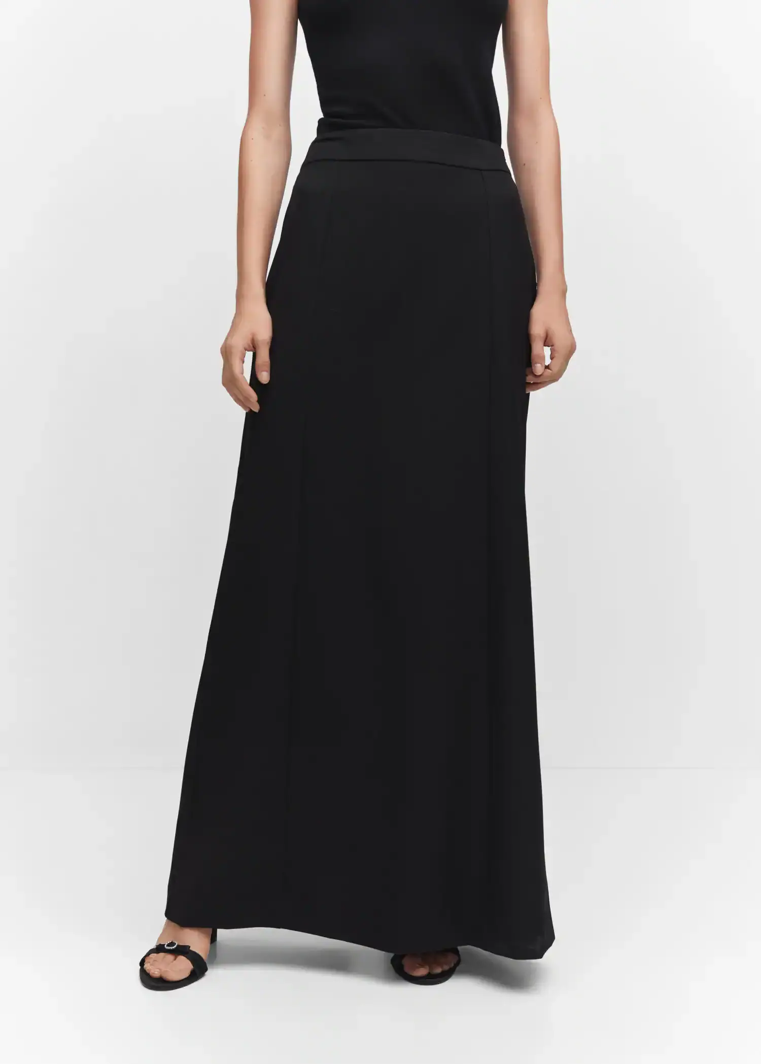 Mango Flowy long skirt. a woman wearing a black dress standing in front of a white wall. 
