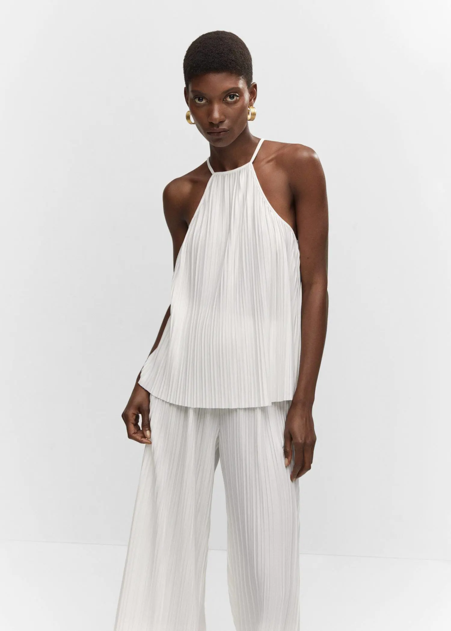 Mango Halter-neck pleated top. a woman in a white outfit standing in front of a wall. 