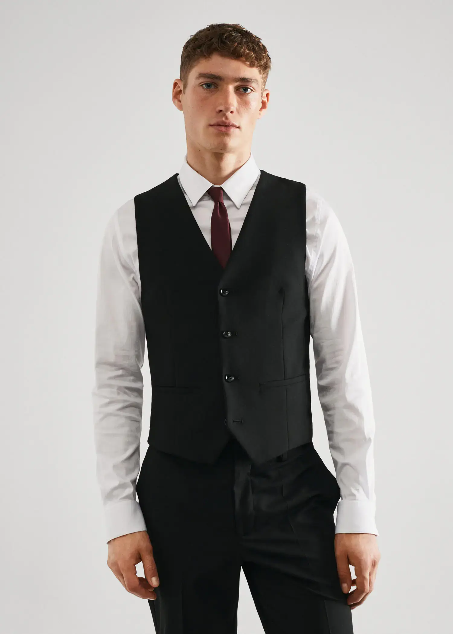 Mango Super slim-fit stretch fabric suit vest. a man wearing a suit and tie standing in front of a white wall. 