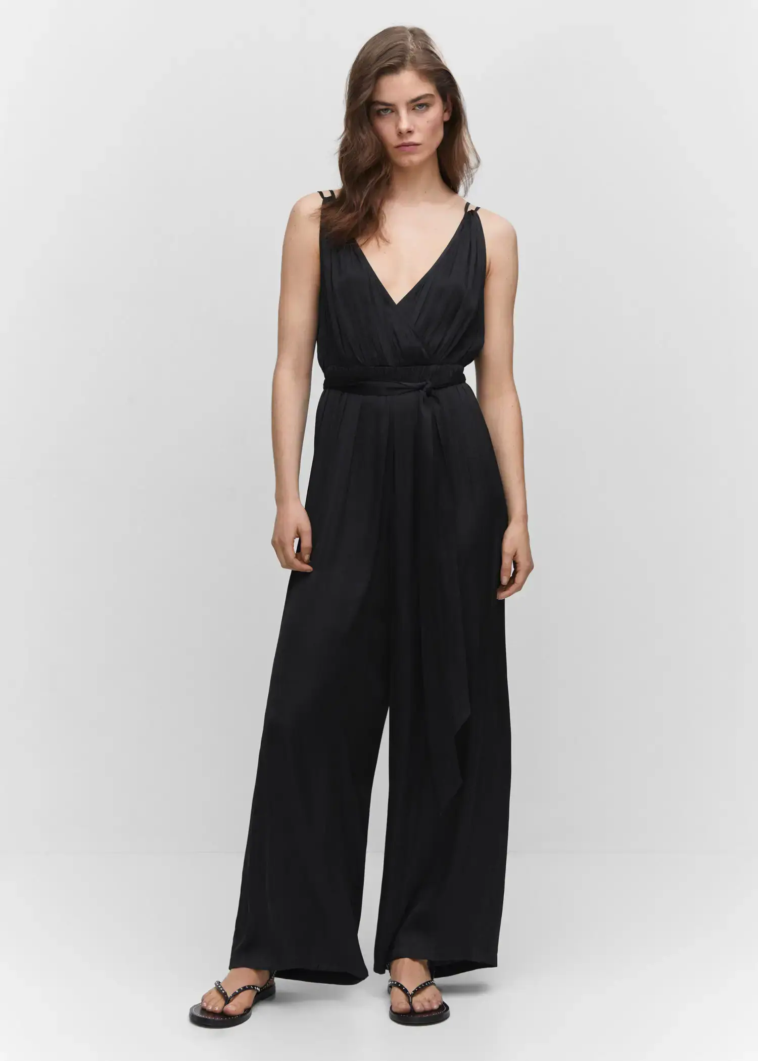 Mango Satin pleated jumpsuit. a woman wearing a black jumpsuit standing in front of a white wall. 