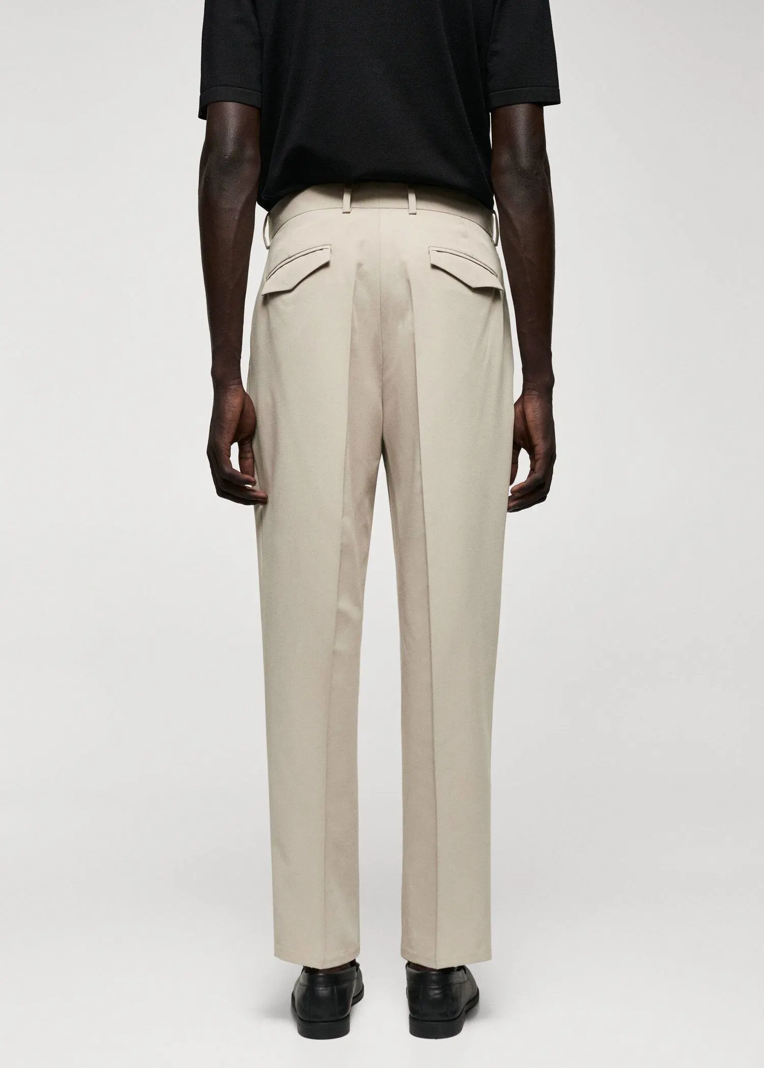 Mango Regular fit suit trousers with pleats. a man wearing a black shirt and beige pants. 