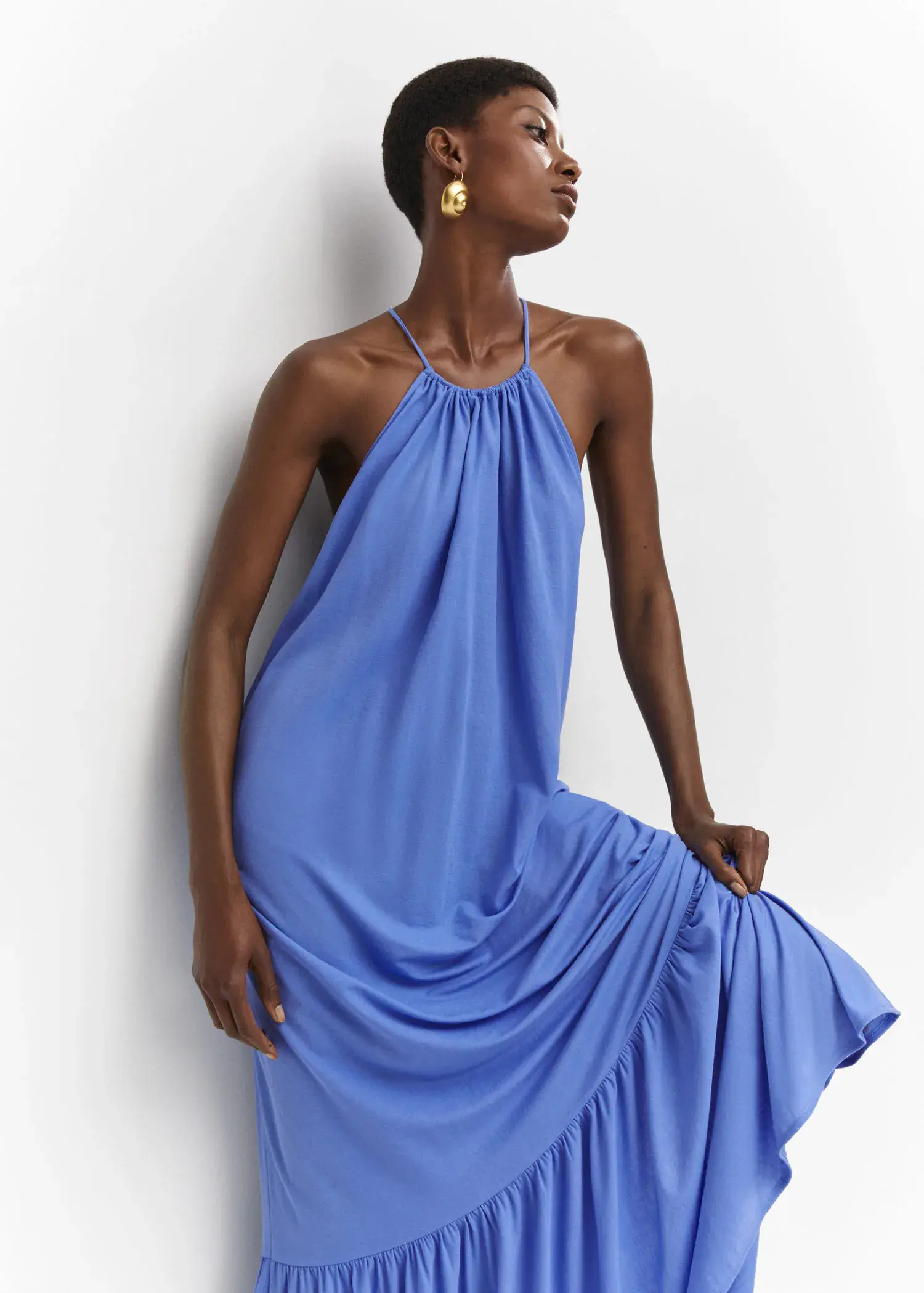 Mango Cross-back maxi-dress. a woman leaning against a wall wearing a blue dress. 