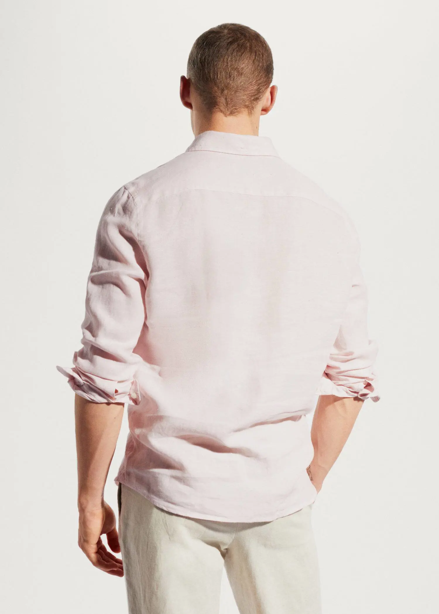 Mango 100% linen slim-fit shirt. a man wearing a light pink shirt with his hands in his pockets. 