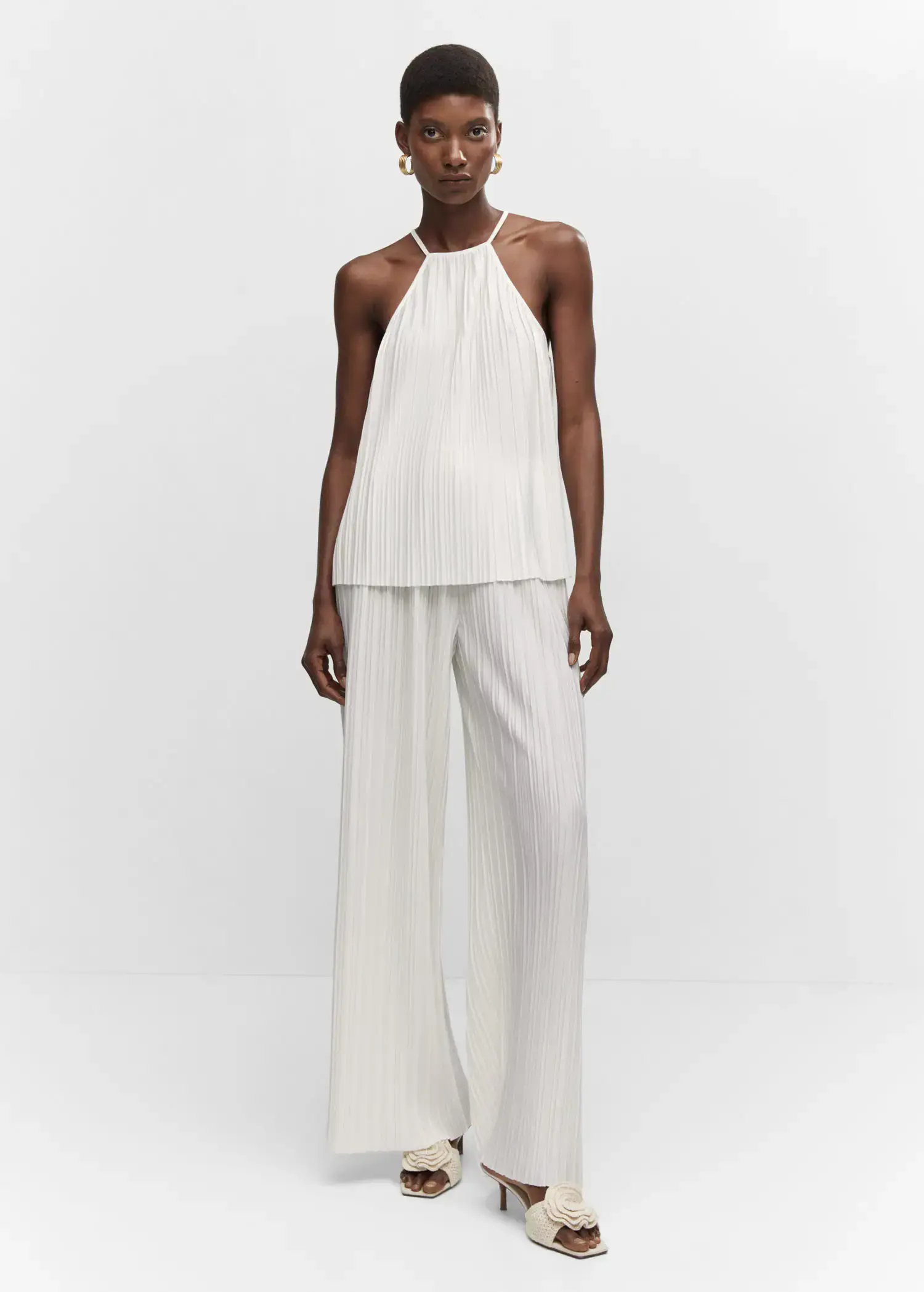 Mango Halter-neck pleated top. a woman standing in a white outfit with her hands in her pockets. 