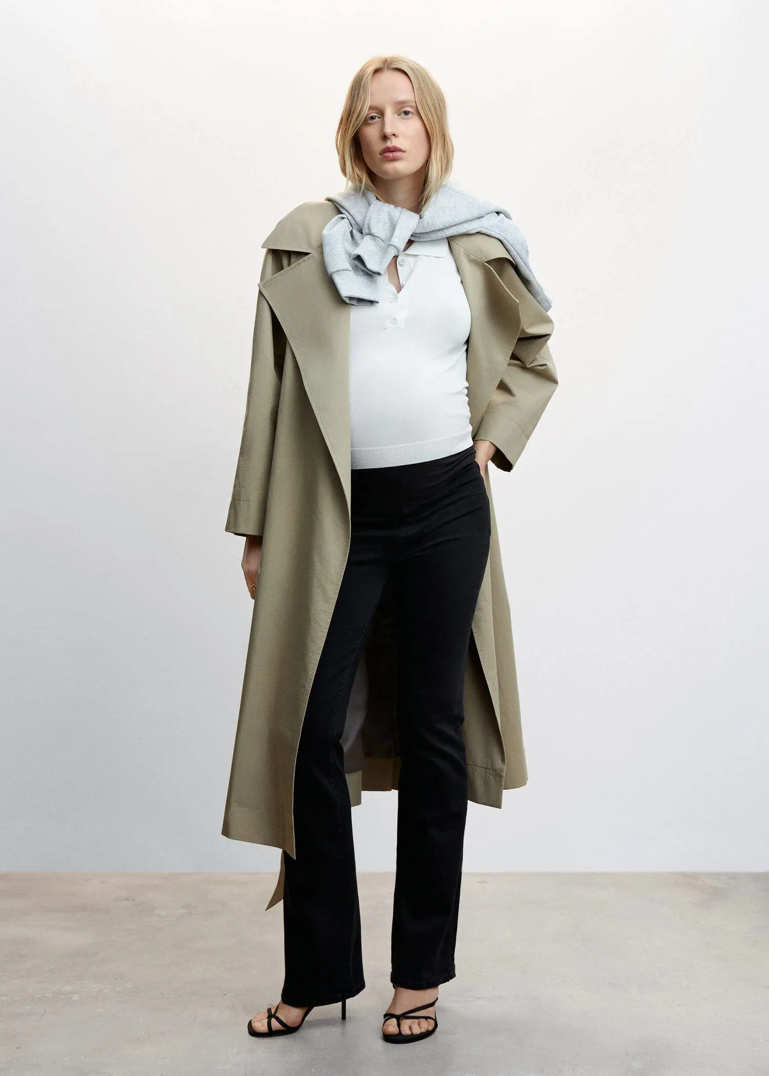 Mango Maternity flared jeans. a woman wearing a trench coat standing in front of a white wall. 
