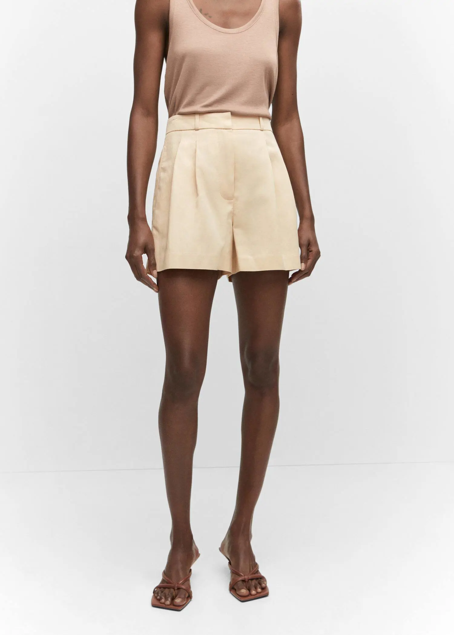 Mango Pleated mid-rise shorts. a person standing in front of a white wall. 
