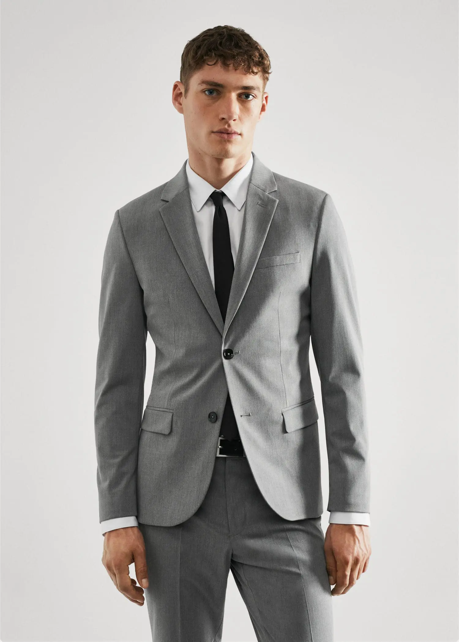 Mango Super slim-fit suit jacket in stretch fabric. a man wearing a suit and tie standing in front of a white wall. 